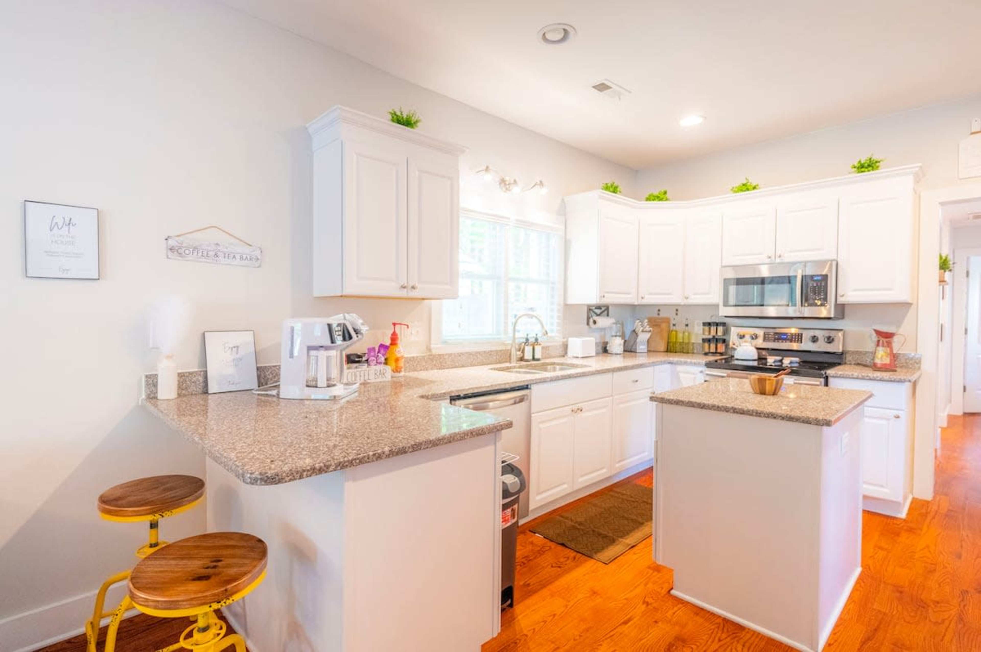 A modern kitchen features white cabinetry, a granite countertop, and stainless steel appliances, with bar stools at the island.