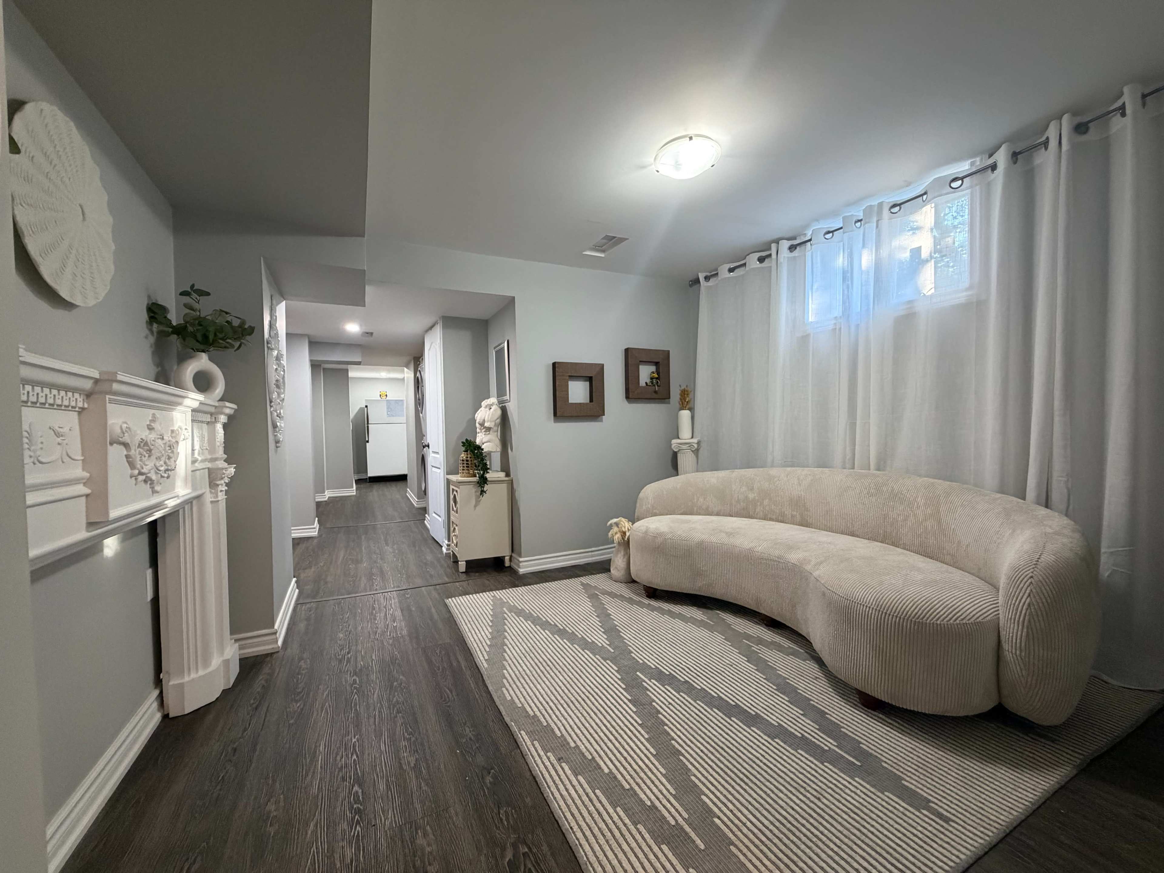 The image shows a well-lit hallway with a curved, beige sofa, a decorative mantel, and several pieces of wall art.