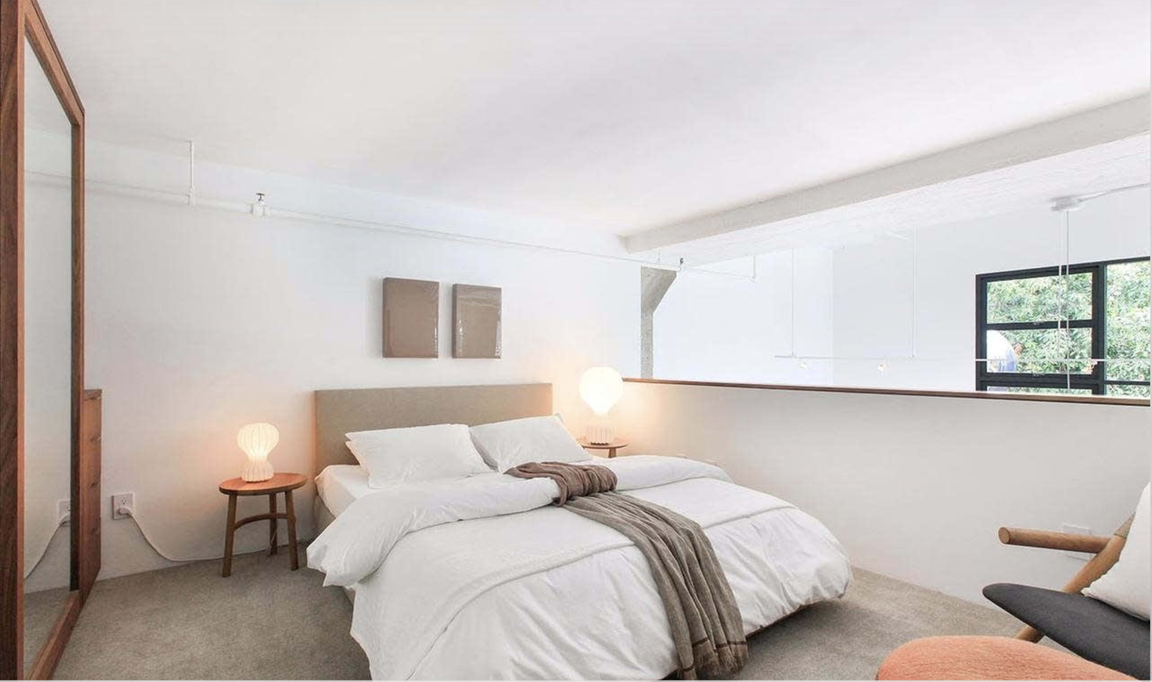 A minimalist bedroom with a bed, nightstand, and large windows allowing natural light.