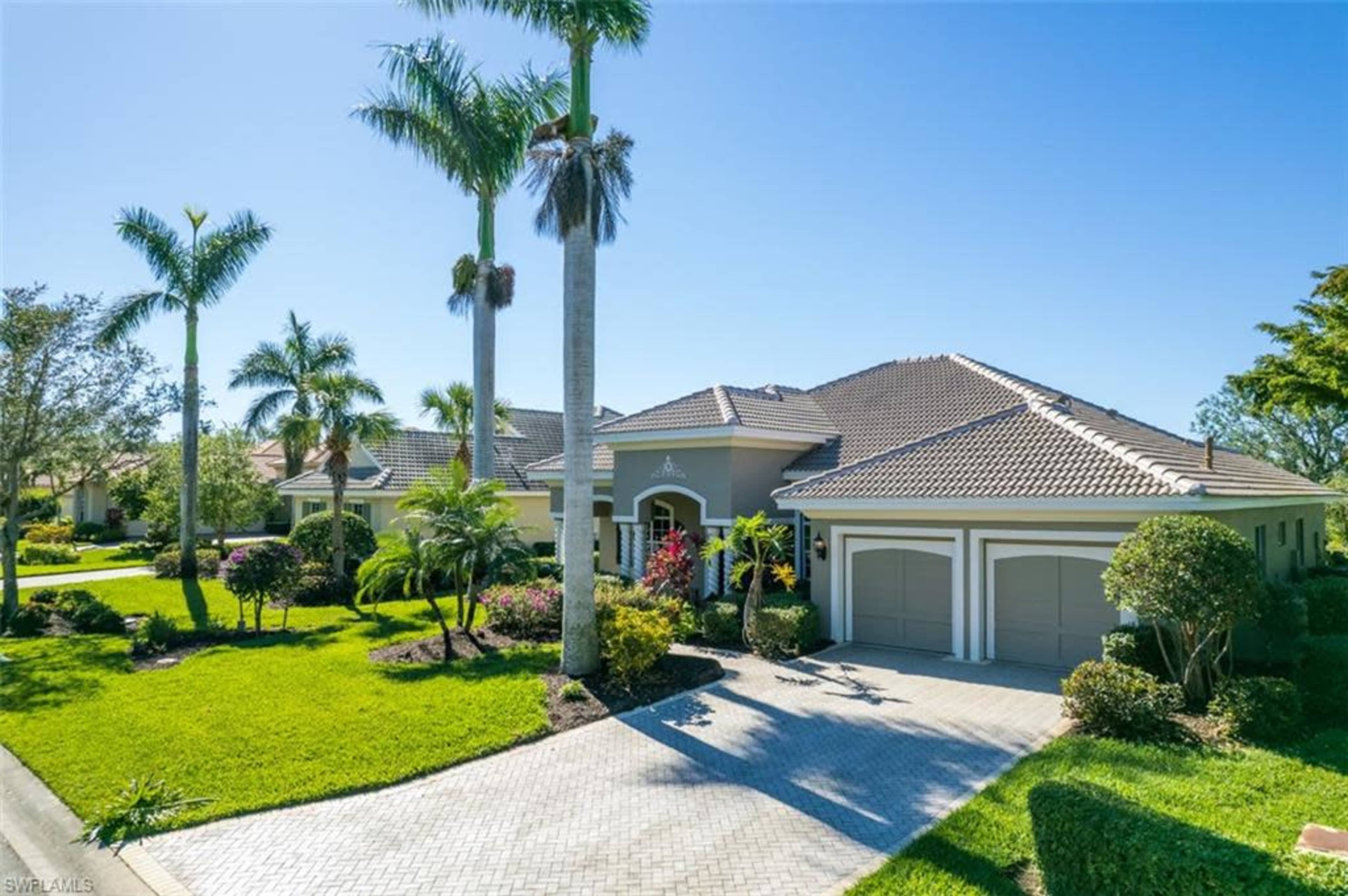 A well-maintained single-story house with a tile roof and a landscaped front yard featuring palm trees and flowering plants.