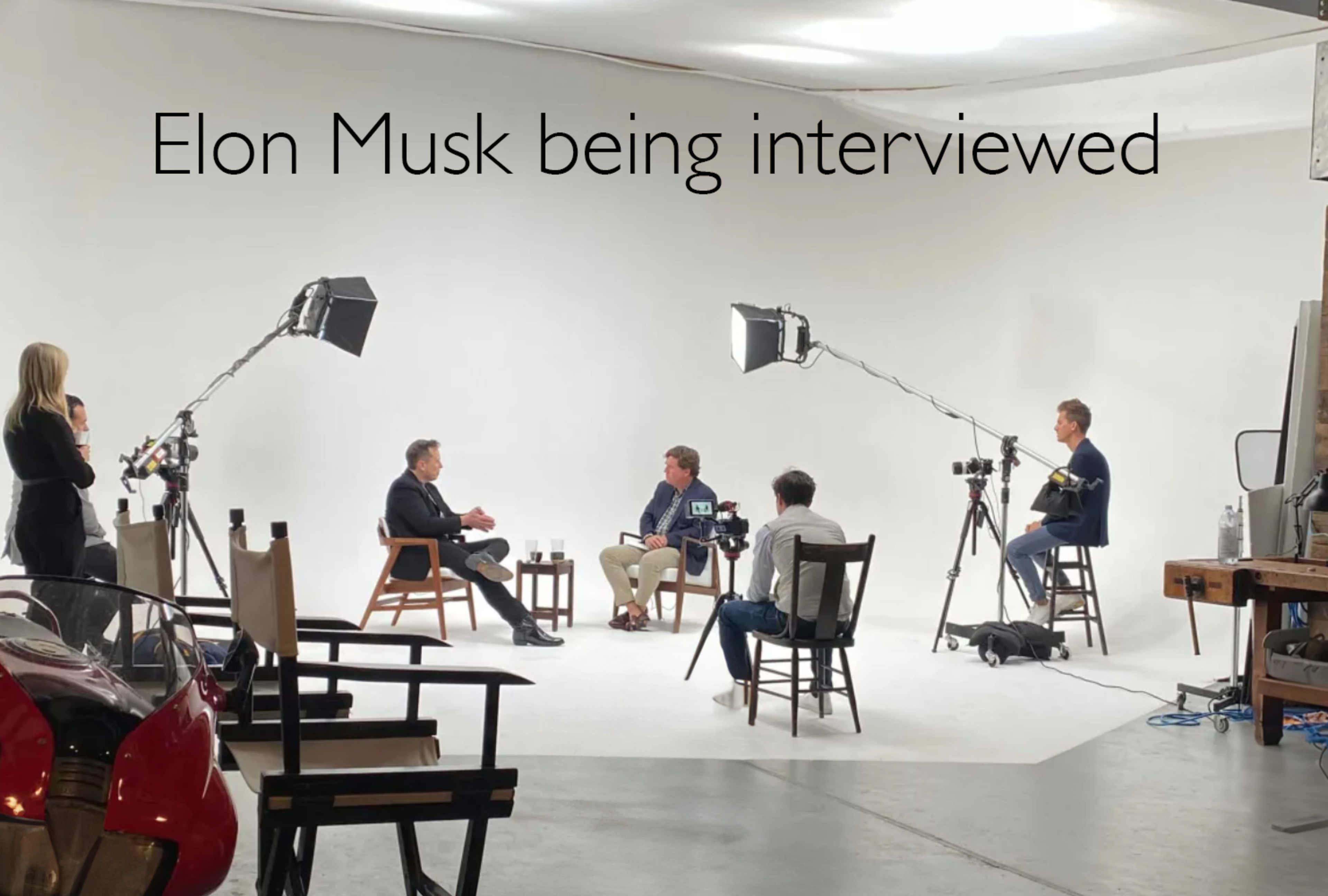 A group of people is seated in a brightly lit studio for an interview, with cameras and lighting equipment set up around them.