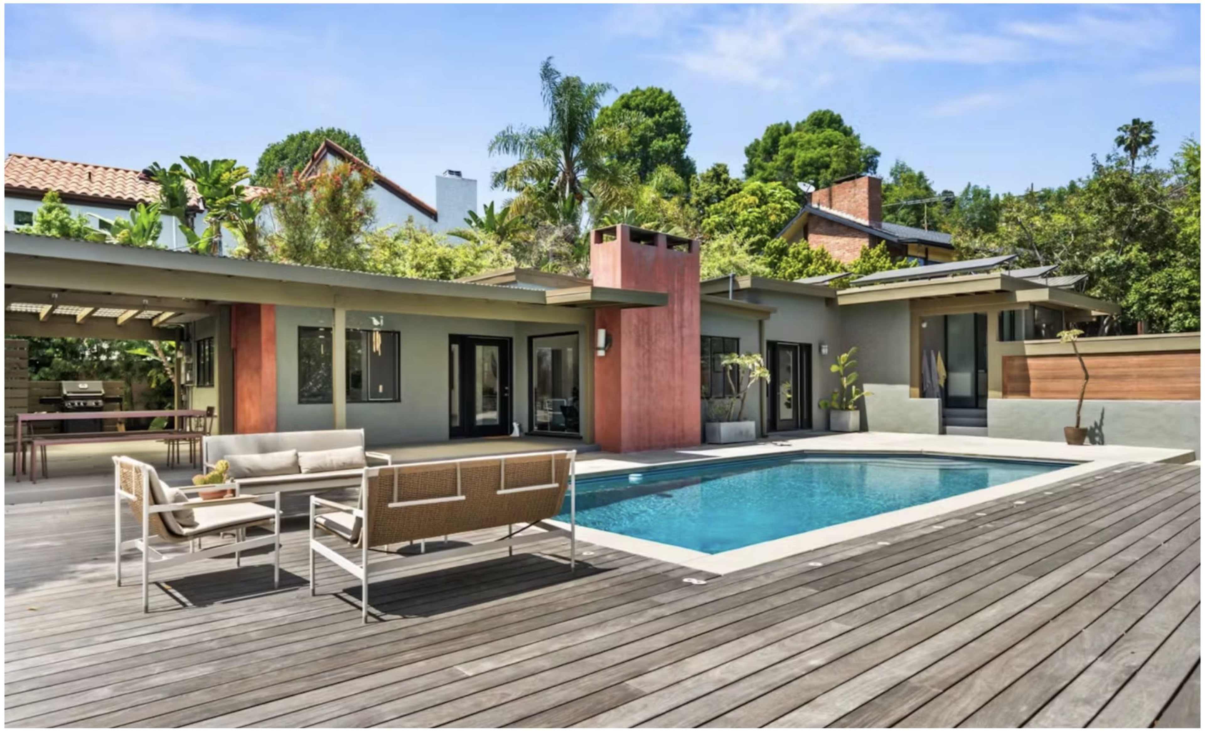 A modern home with a swimming pool surrounded by wooden decking and tropical landscaping.