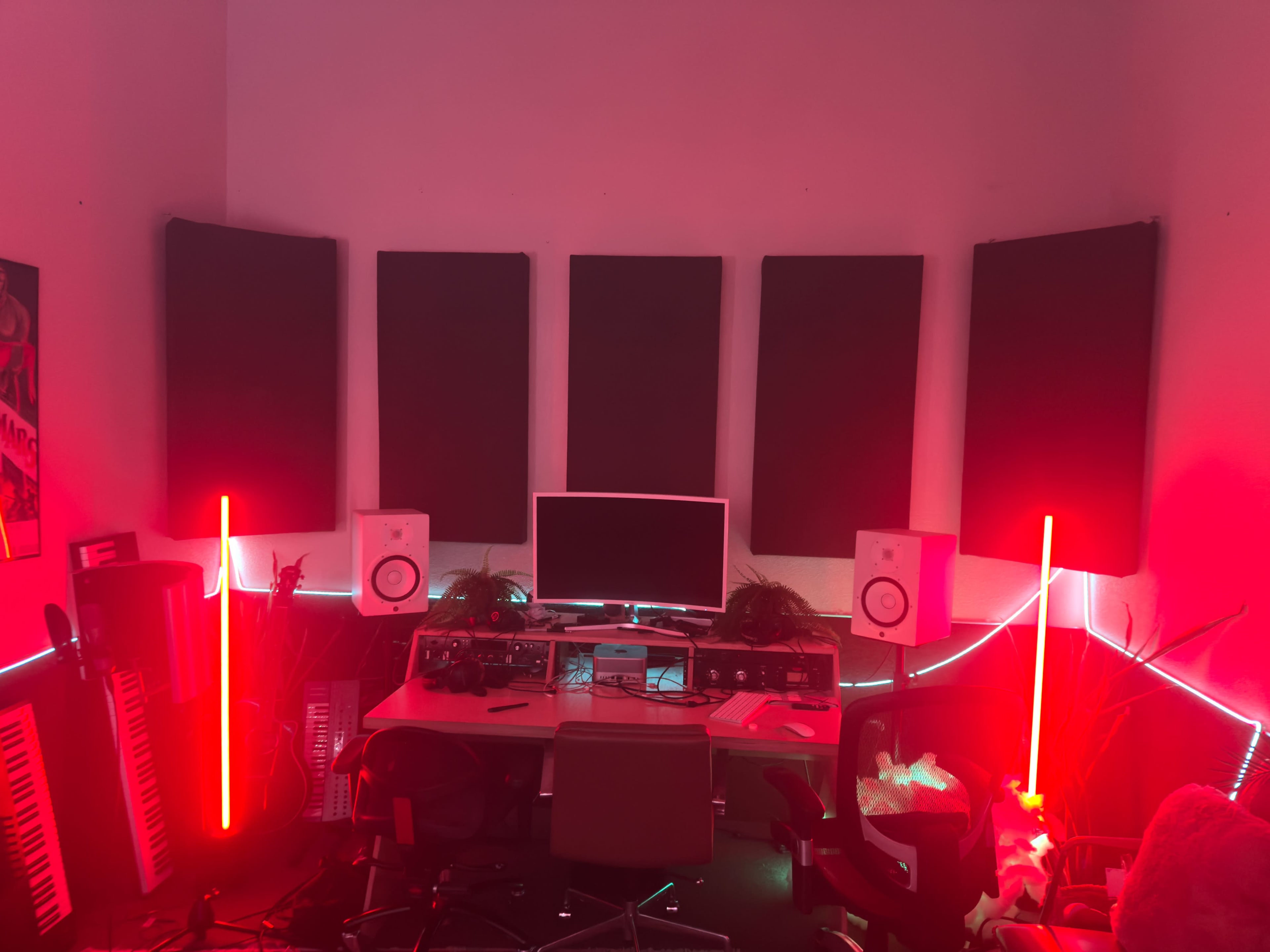 The image shows a music studio with a desk, a computer monitor, speakers, soundproof panels on the walls, and neon lighting.
