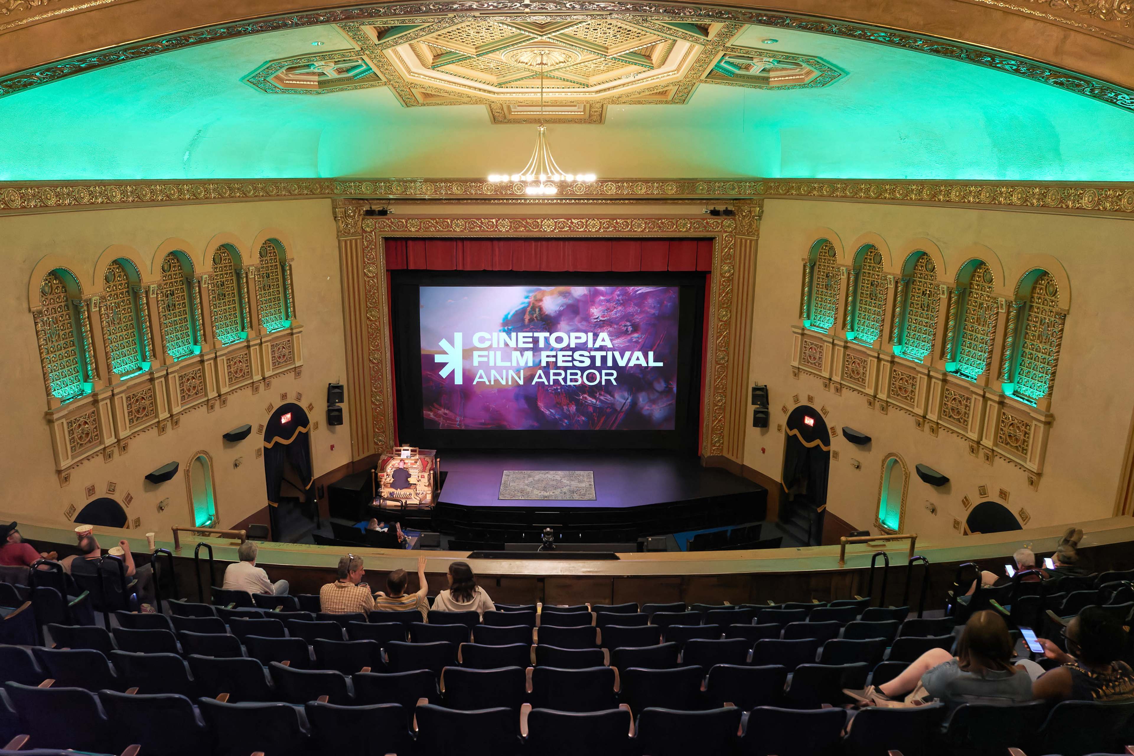 The image shows a theater auditorium set up for the Cinetopia Film Festival in Ann Arbor, featuring a large screen on stage and rows of empty seats.