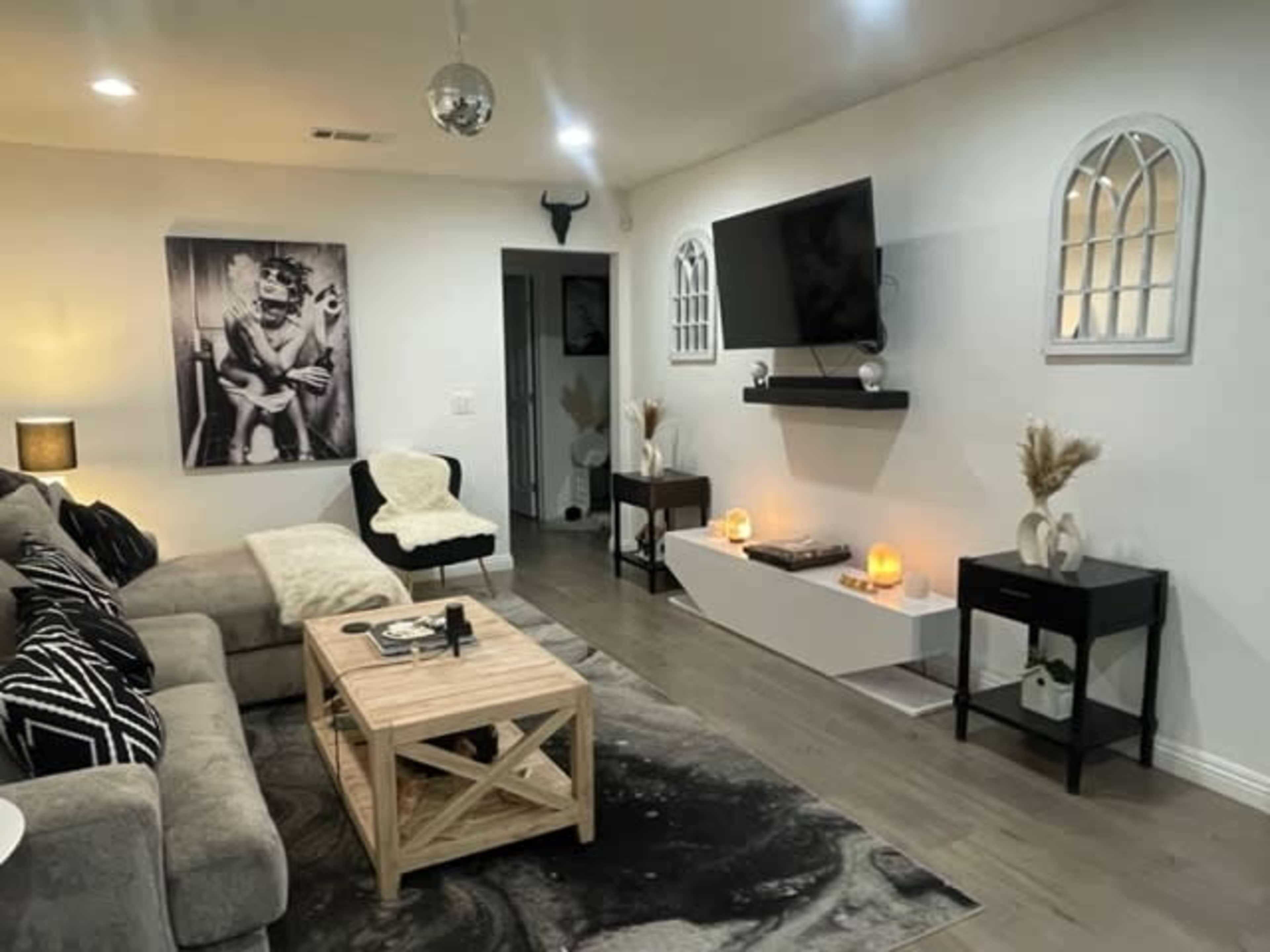 A living room with a gray sectional sofa, a wooden coffee table, a large wall-mounted TV, and decorative accents like candles and framed art.