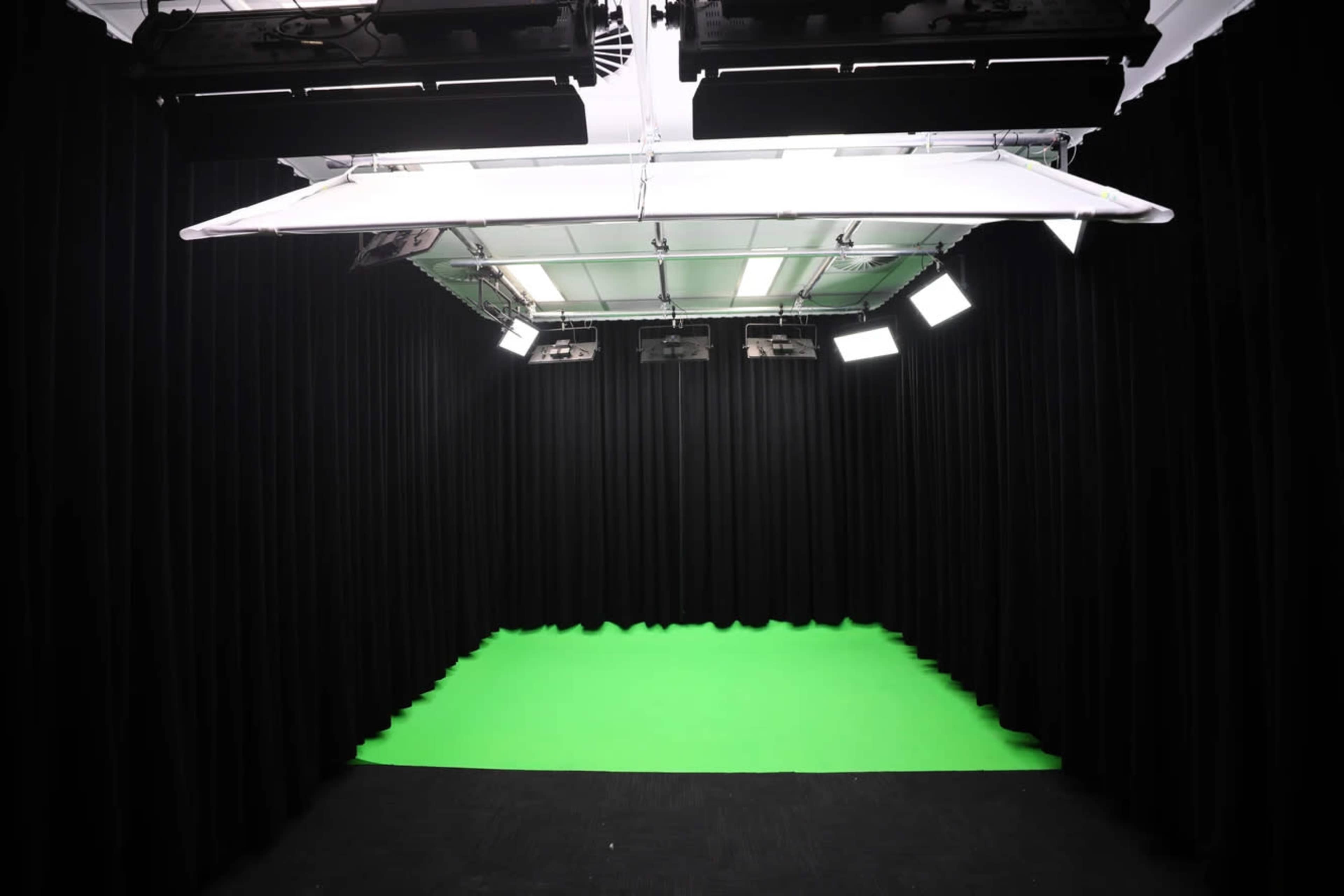 The image shows a photography studio with black curtains and a green screen set up on the floor.