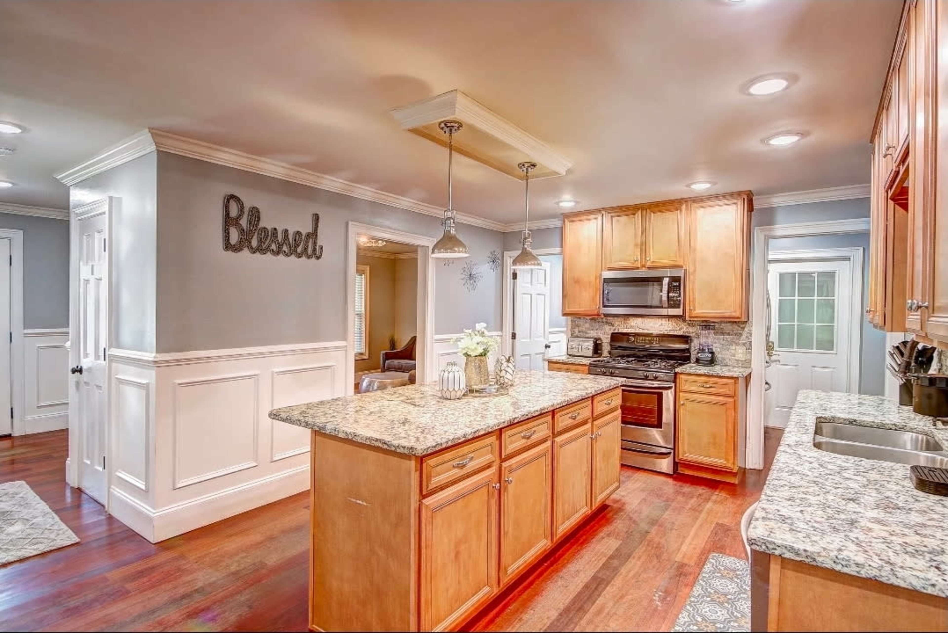 A modern kitchen features wooden cabinets, granite countertops, and stainless steel appliances, with a decorative "Blessed" sign on the wall.