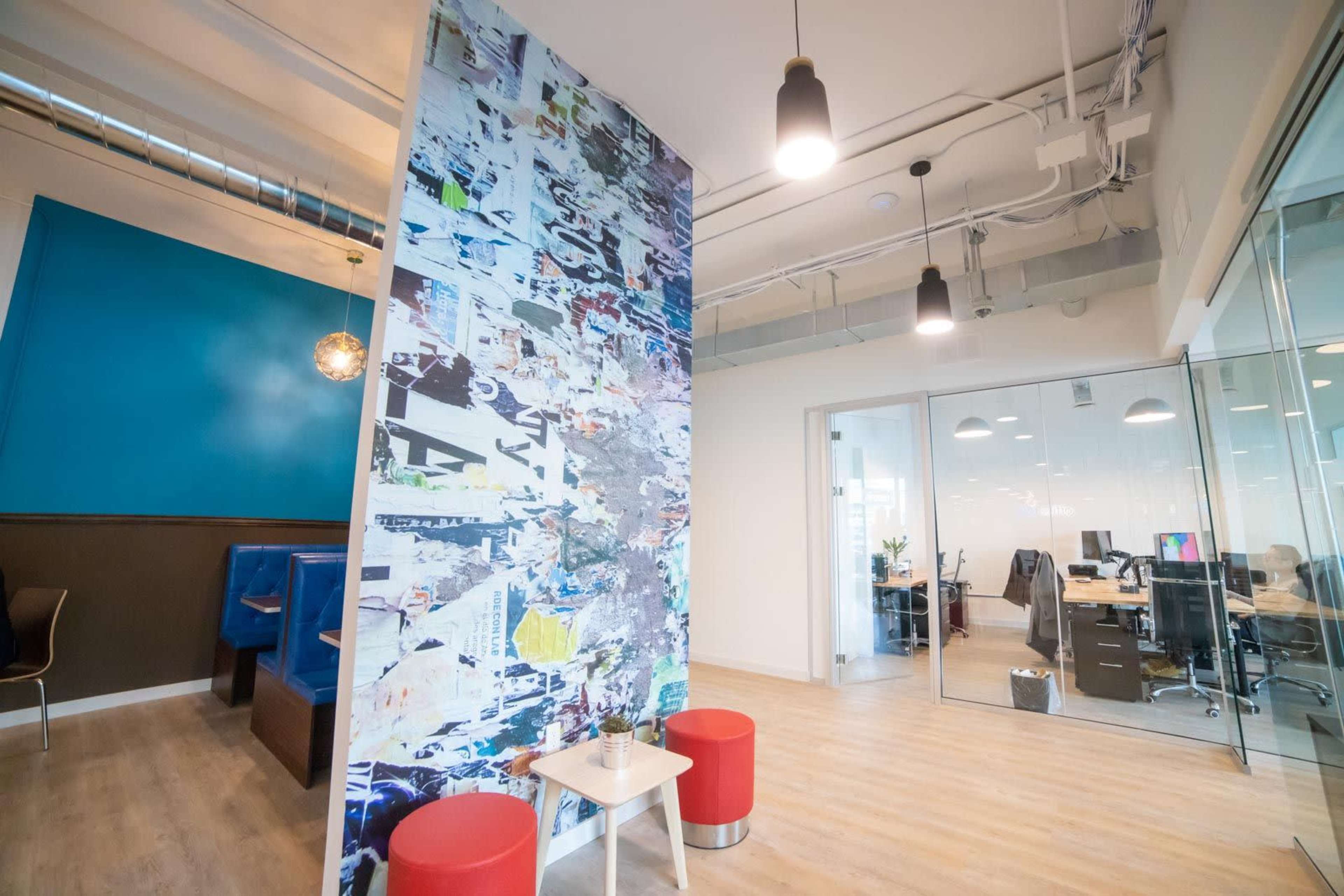 A modern office interior with a decorative wall, two red stools, and glass-walled workspaces in the background.