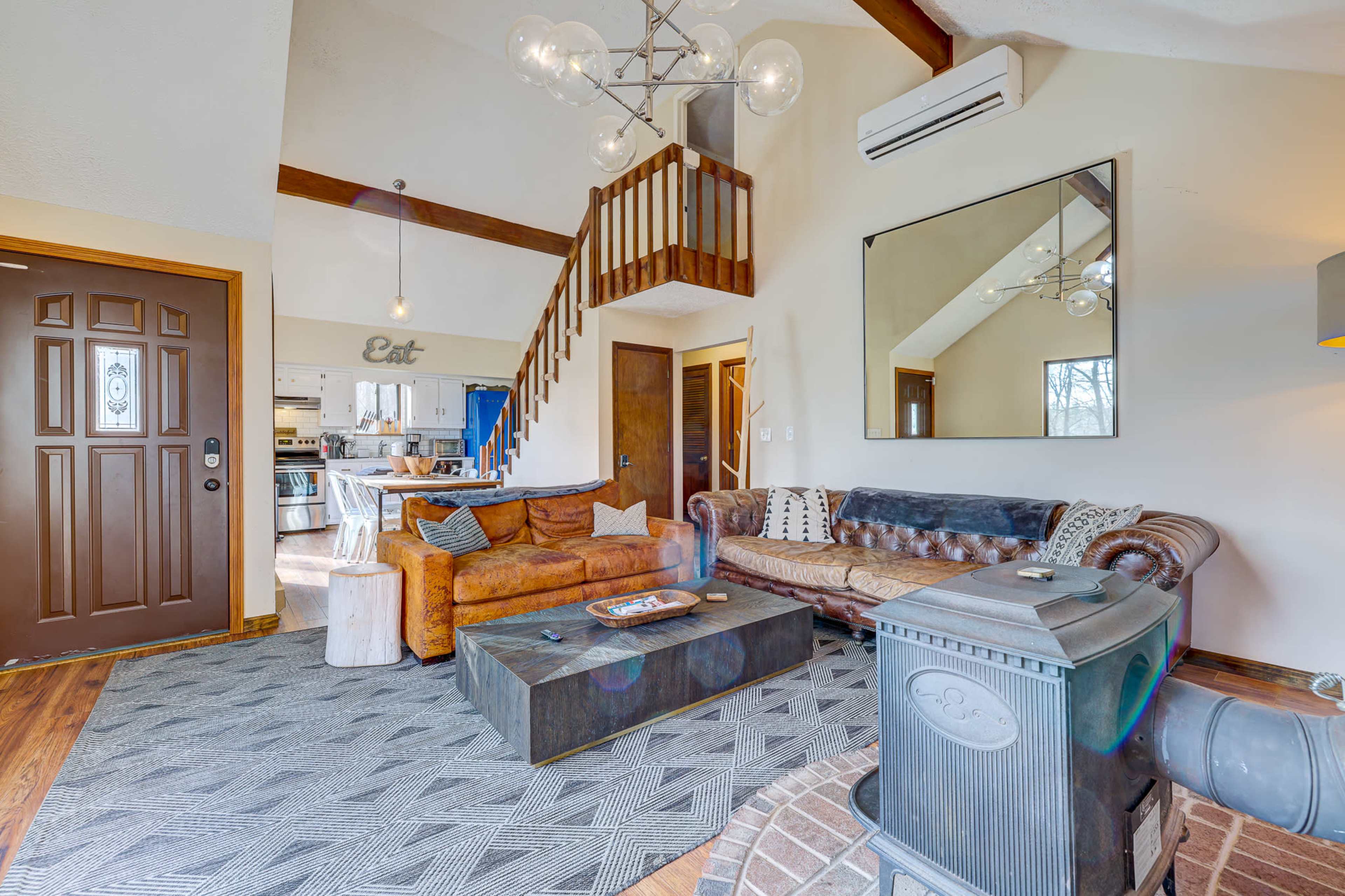 The image shows a cozy living room with a mix of modern and rustic furnishings, featuring a leather sofa, a coffee table, and a staircase leading to an upper level.