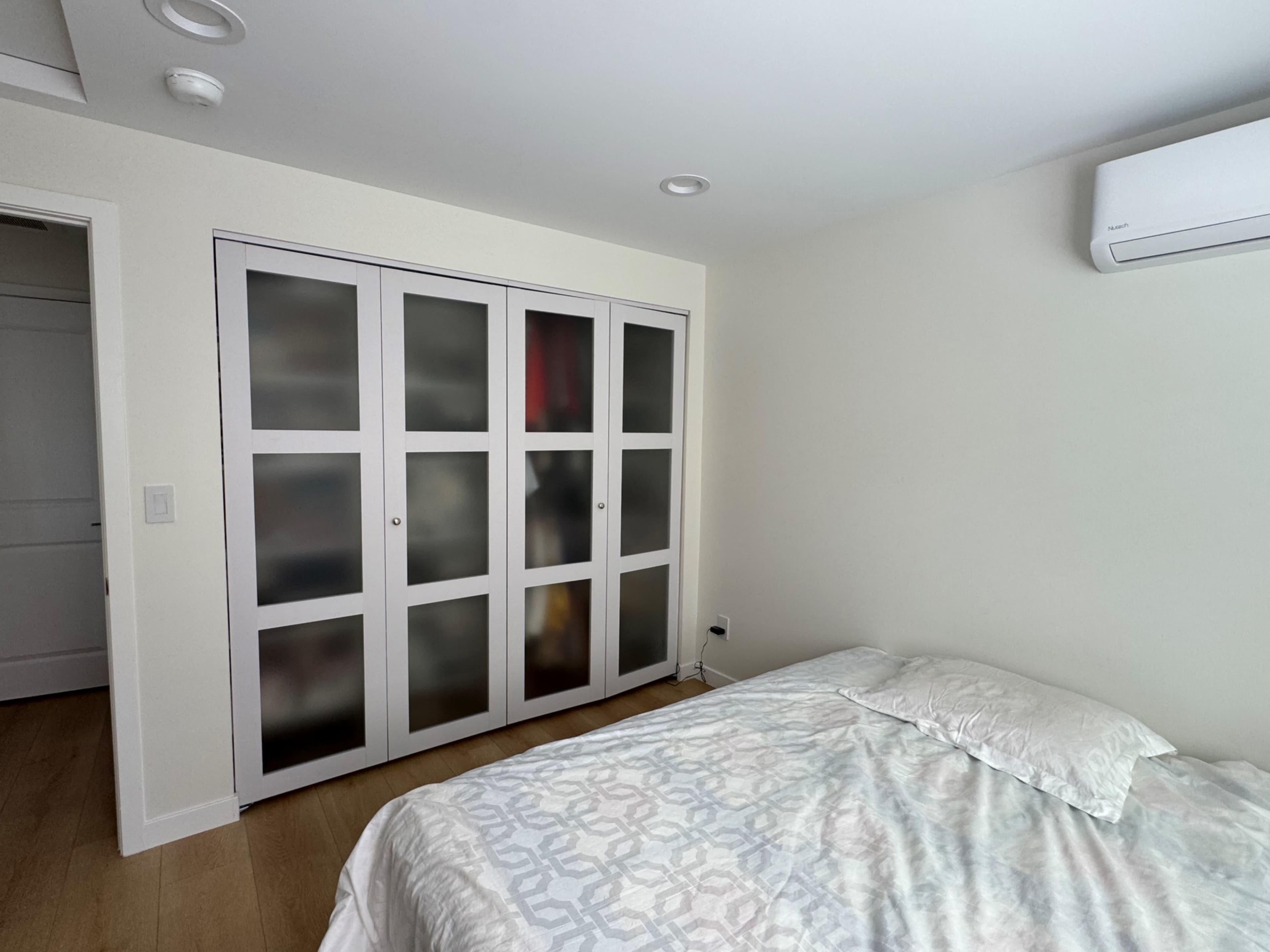 The image shows a bedroom with a bed and a closet featuring frosted glass doors.