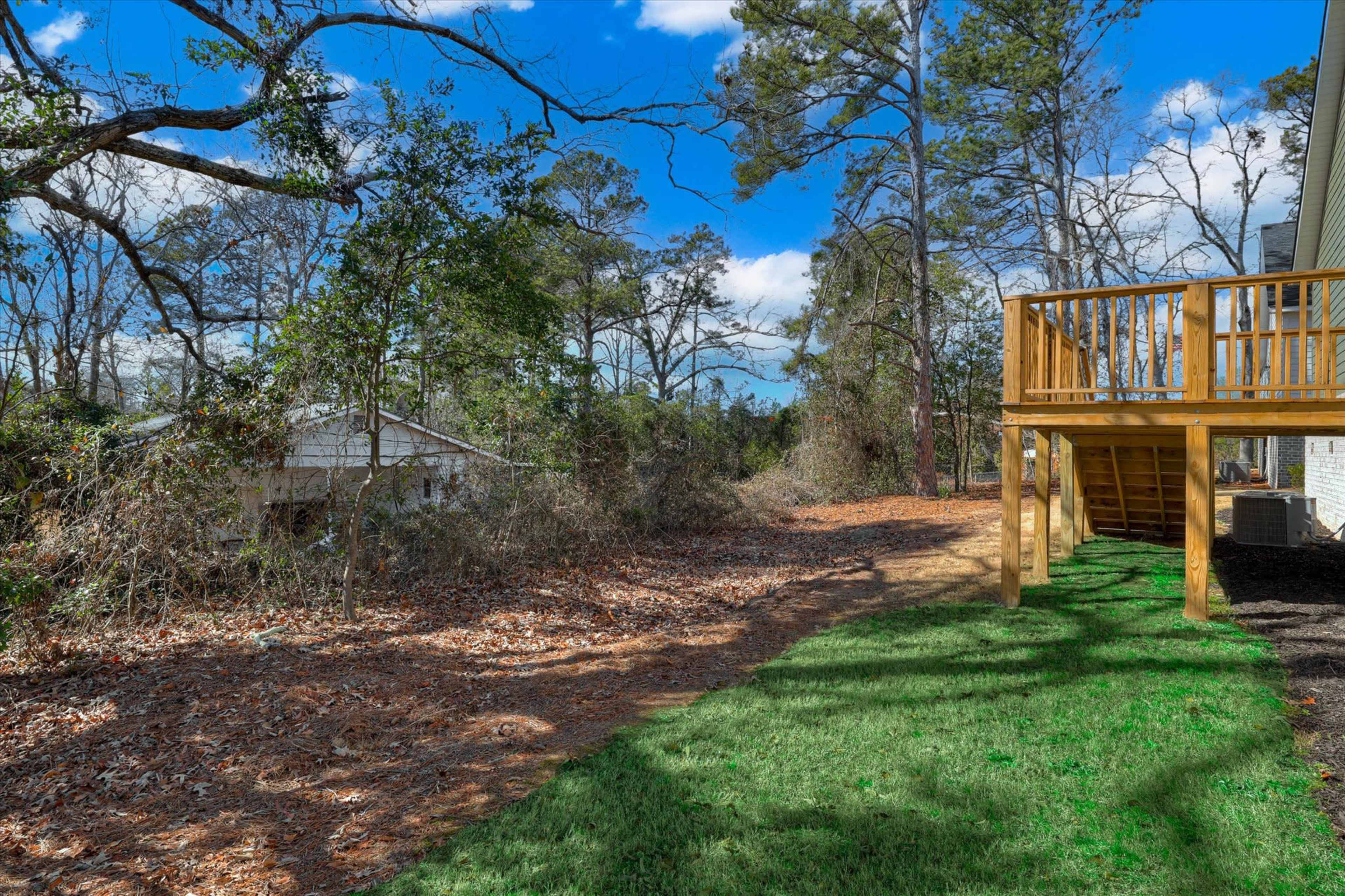 The image shows a wooden deck extending from a house, with a grassy area and overgrown vegetation in the background.