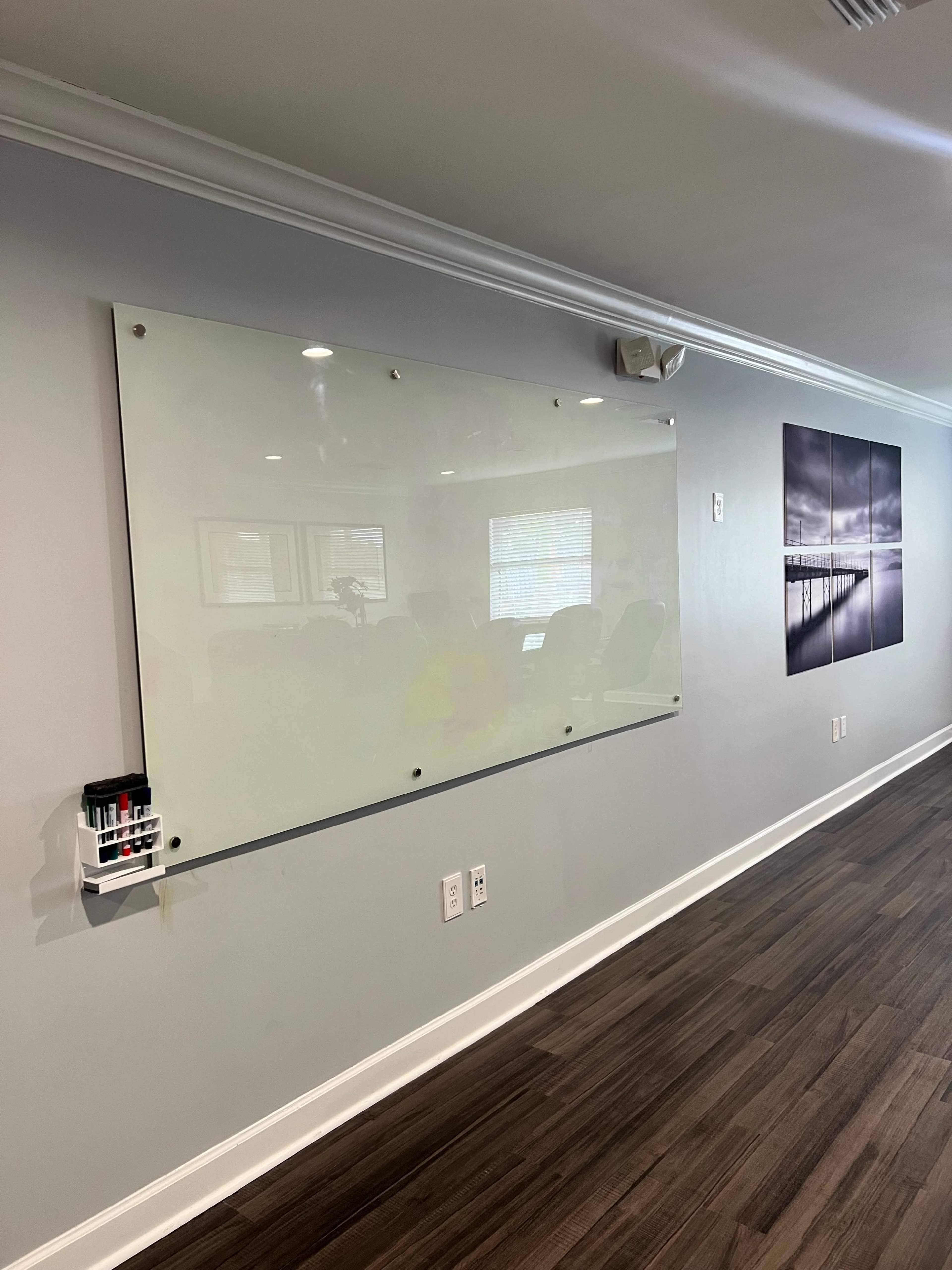A clear whiteboard mounted on a gray wall, beside a panel of framed photographs depicting a pier.