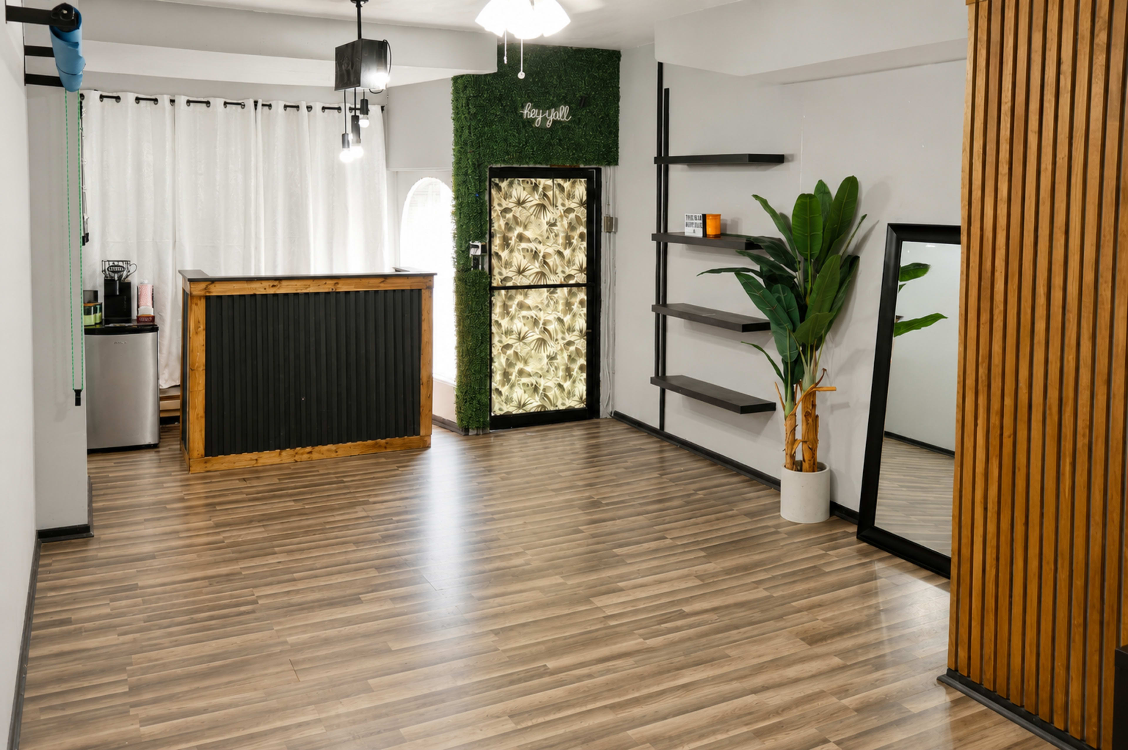 The image shows a modern, minimalist interior space with a wooden bar counter, potted plant, and a large mirror against wooden wall paneling.