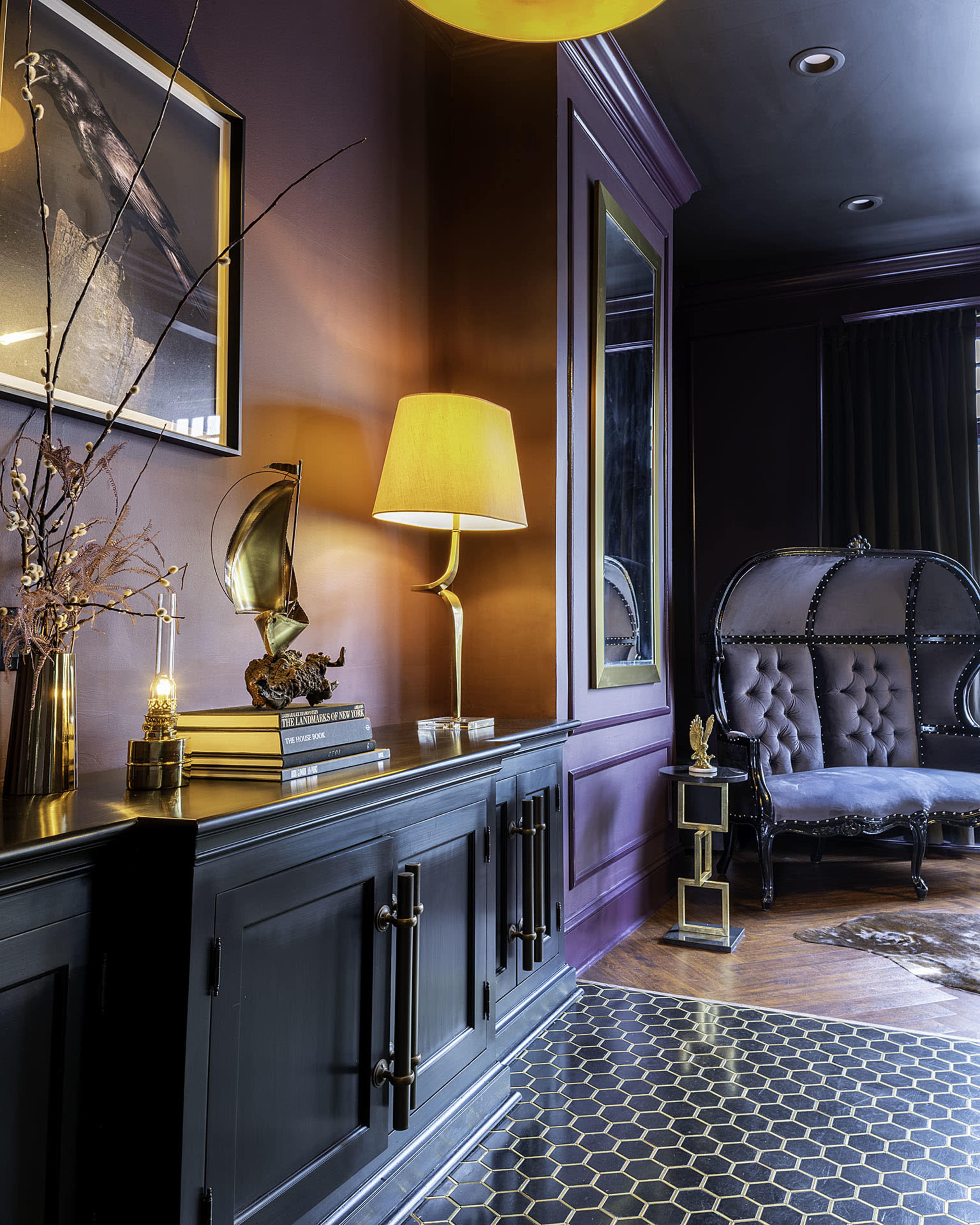 A stylish interior featuring a dark wall, a decorative cabinet, a lamp, and a vintage-style chair.
