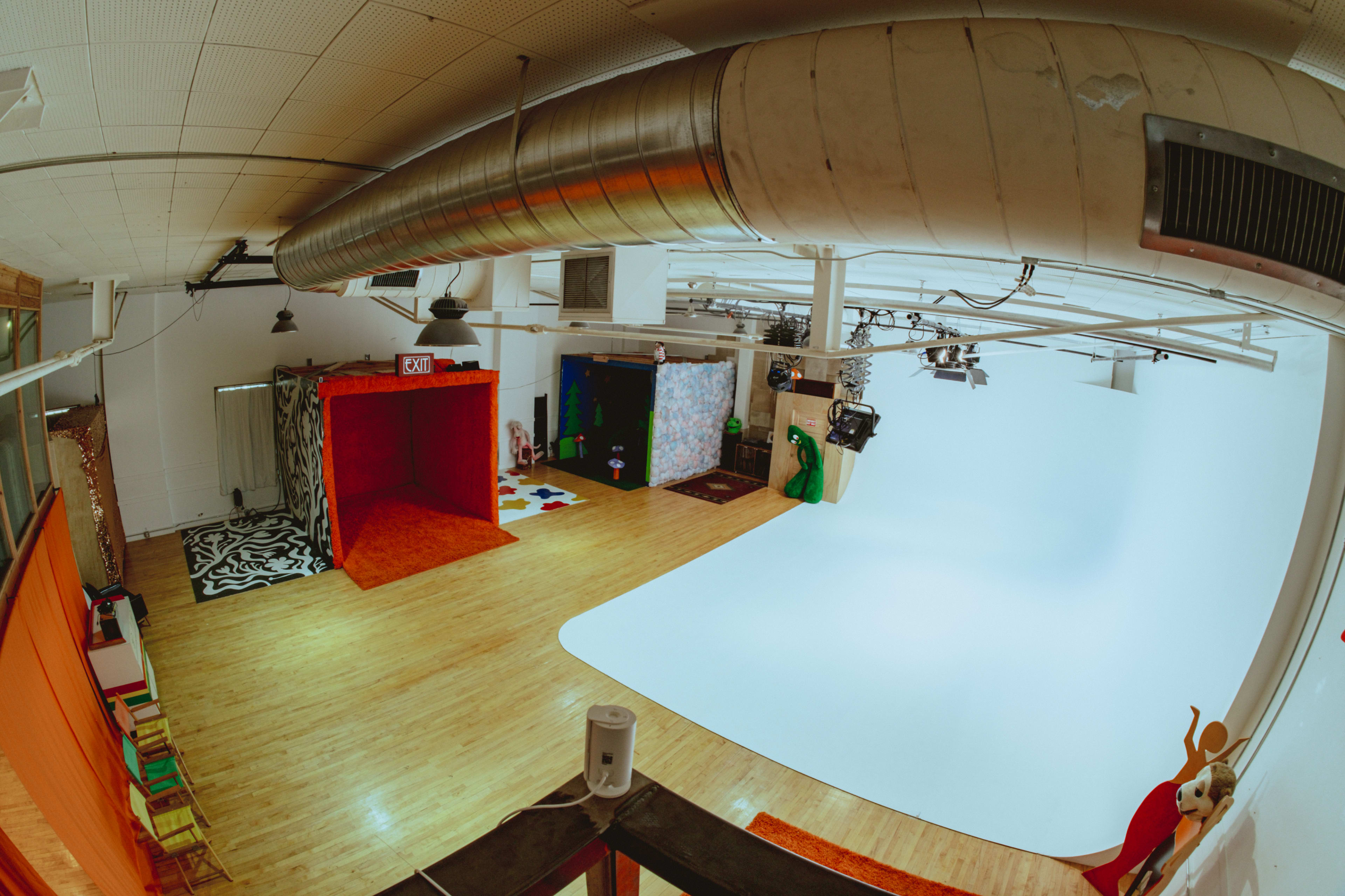 The image shows a spacious studio with multiple colorful backdrops, wooden flooring, and various props arranged throughout the area.