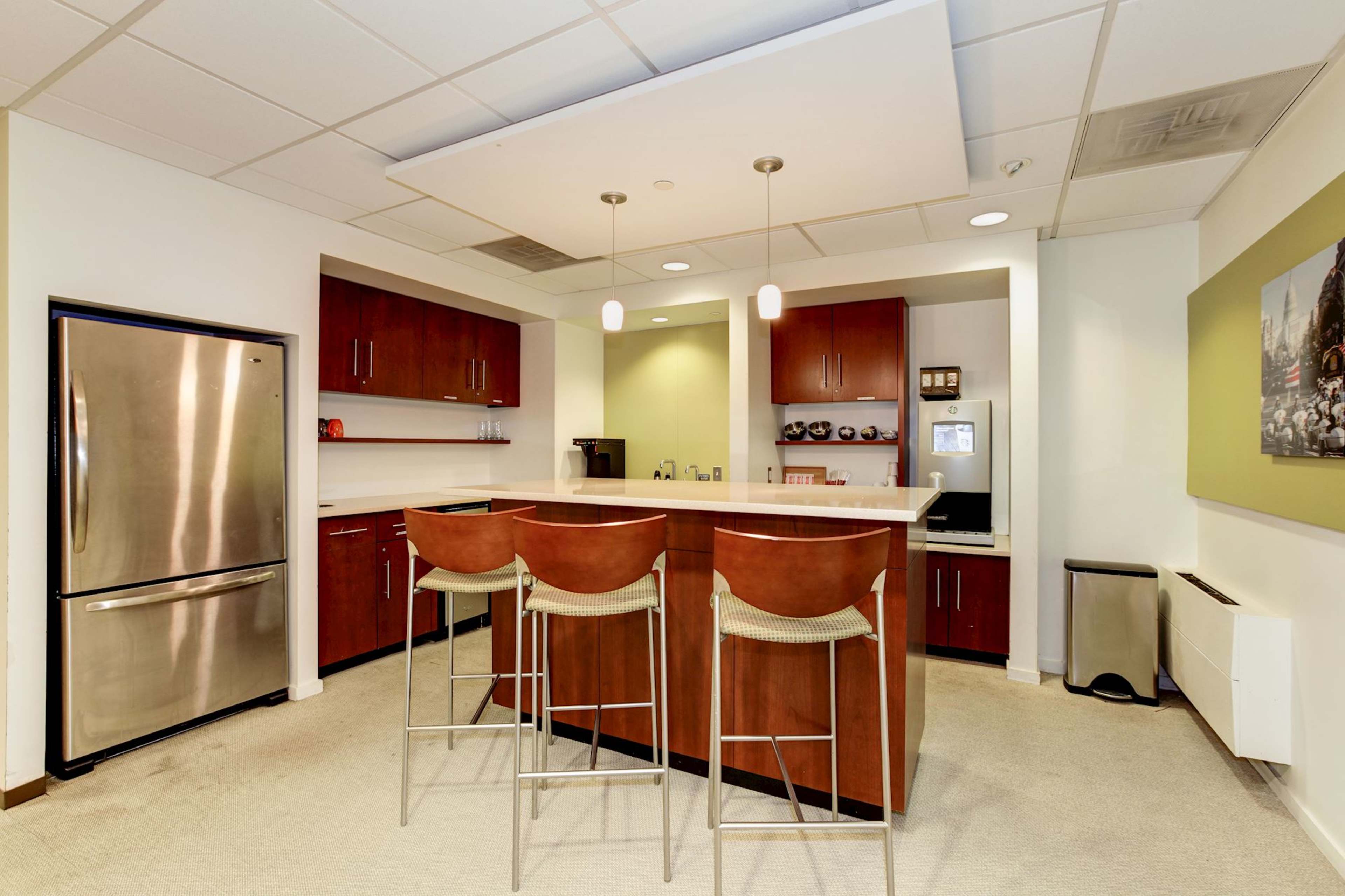 A modern kitchen with wooden cabinetry, a stainless steel refrigerator, and four bar stools at a counter.