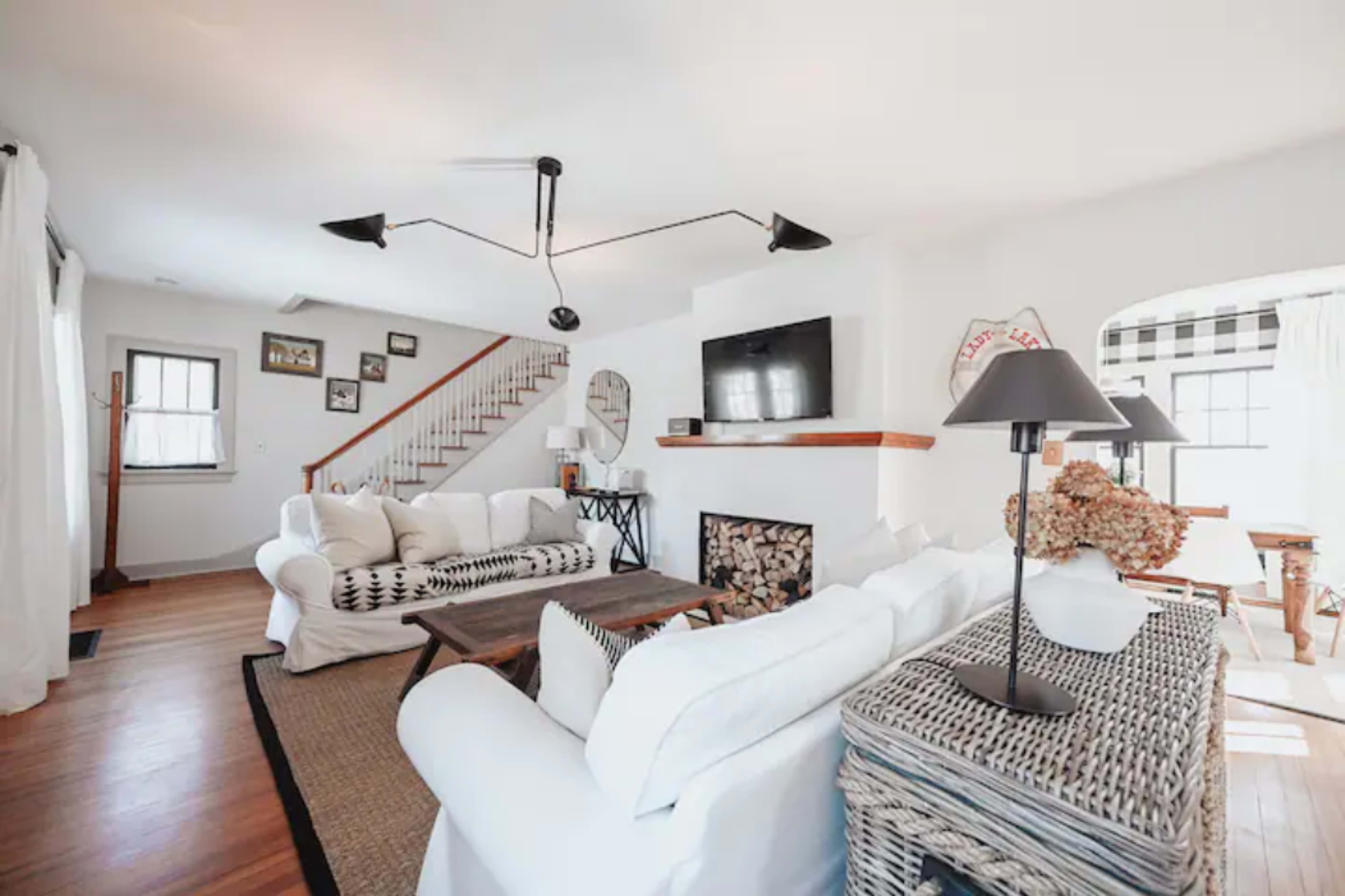 The living room features a white sectional sofa, a wooden coffee table, a fireplace, and a staircase in the background.