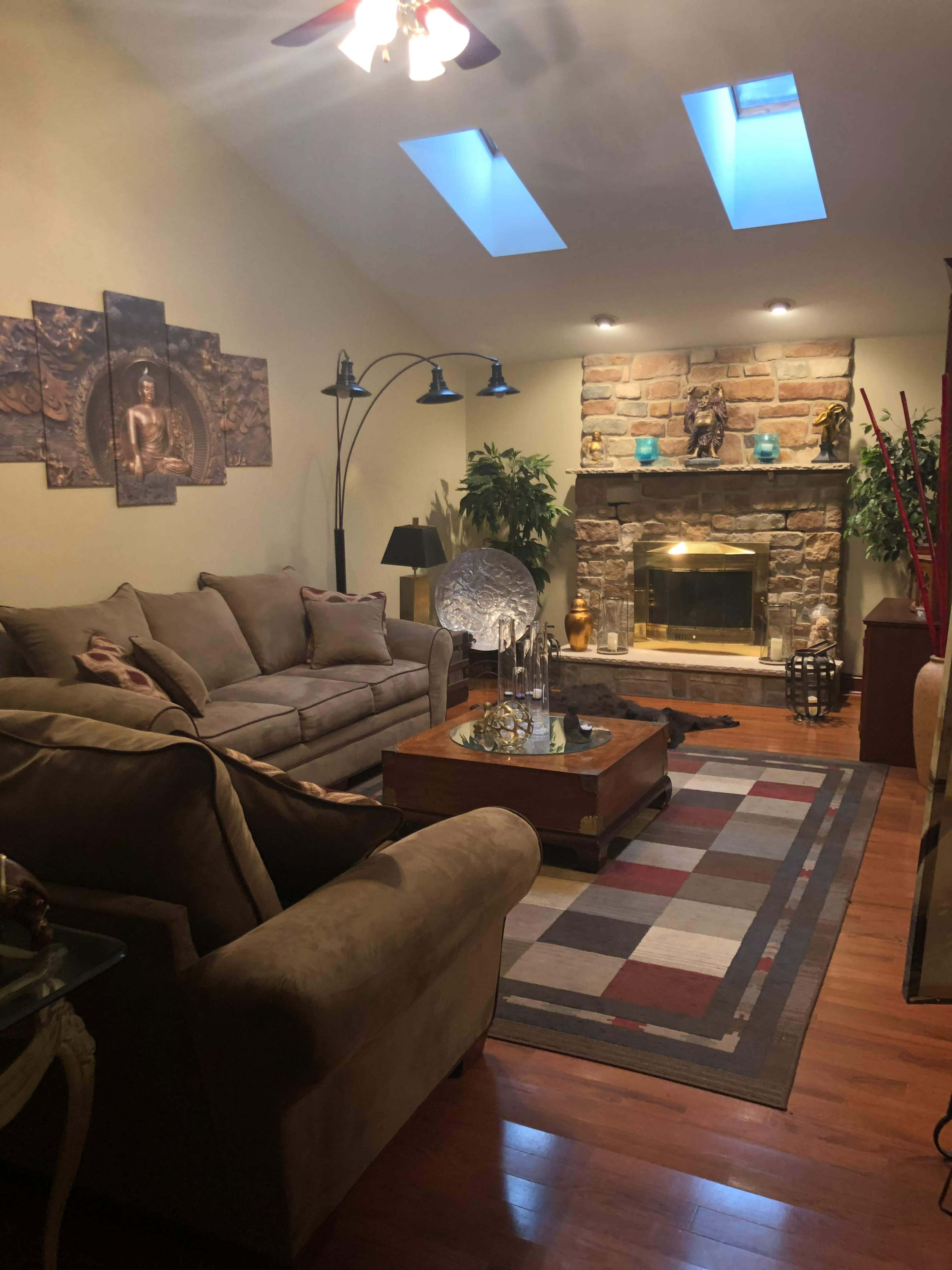 The room features a cozy seating arrangement with a large sofa, a coffee table, and a stone fireplace, illuminated by natural light through skylights.