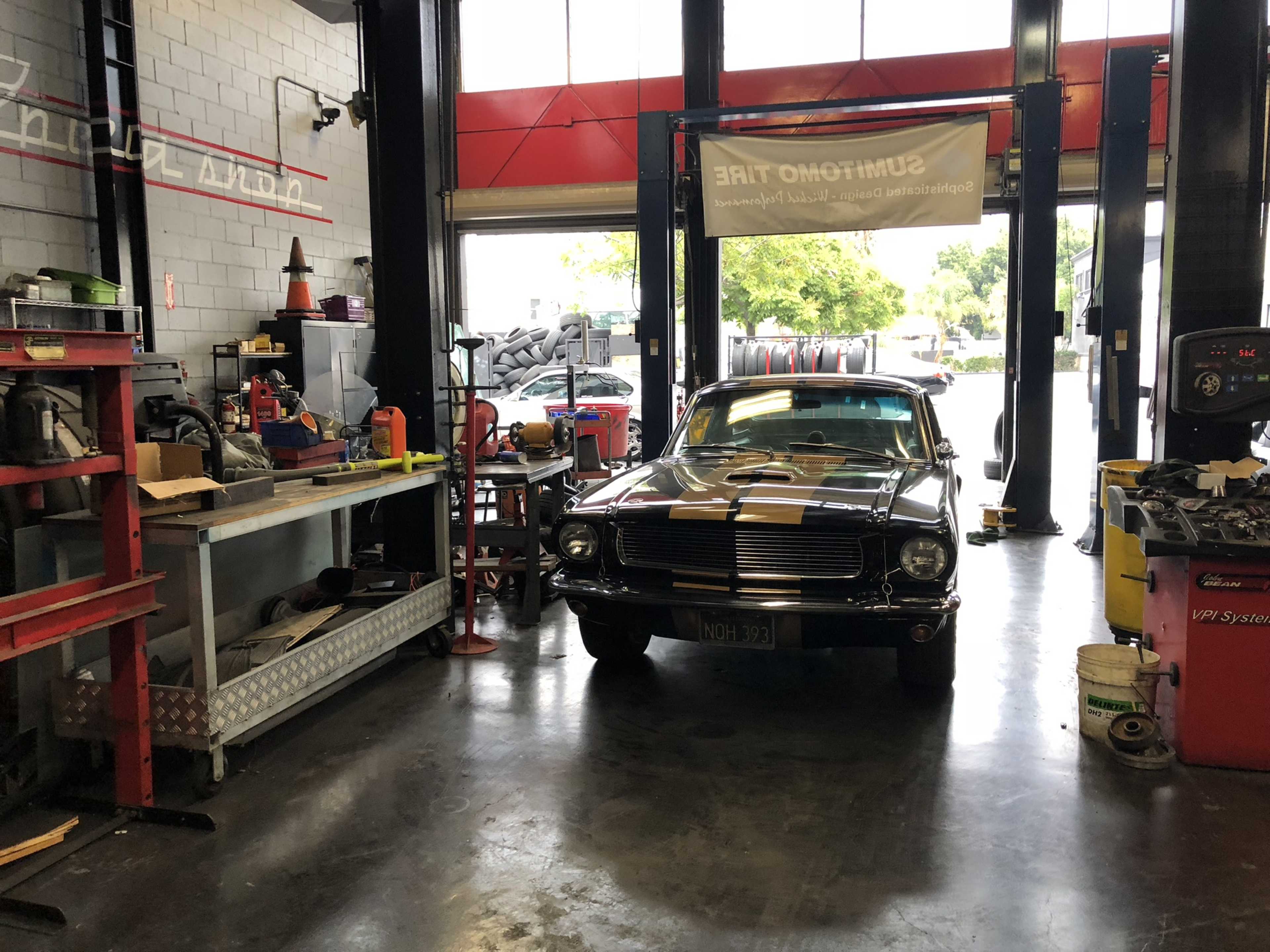 A classic car is parked inside a tire shop, surrounded by various tools and equipment along the walls.