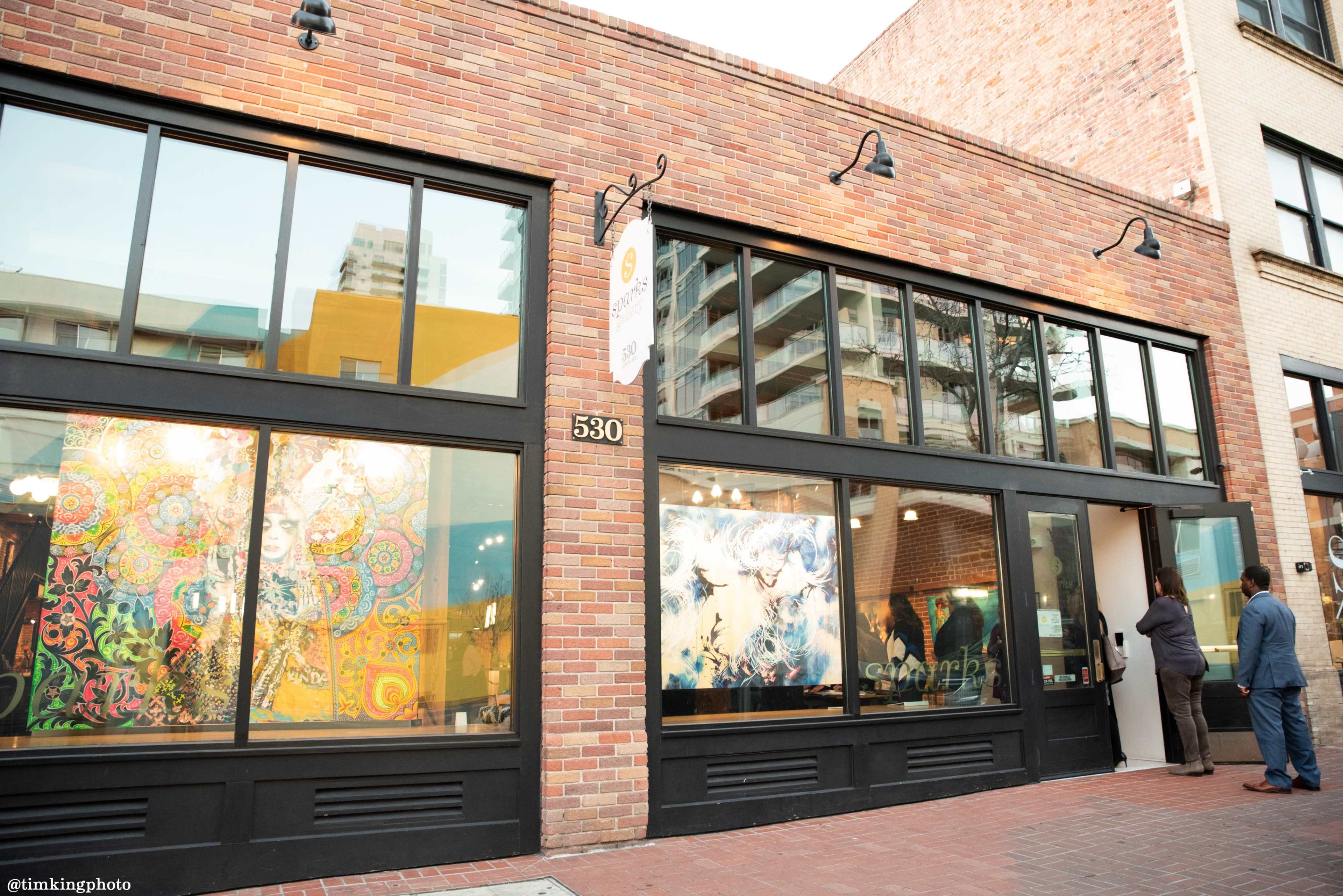 A brick building with large windows displaying colorful artwork and a person entering through the door.