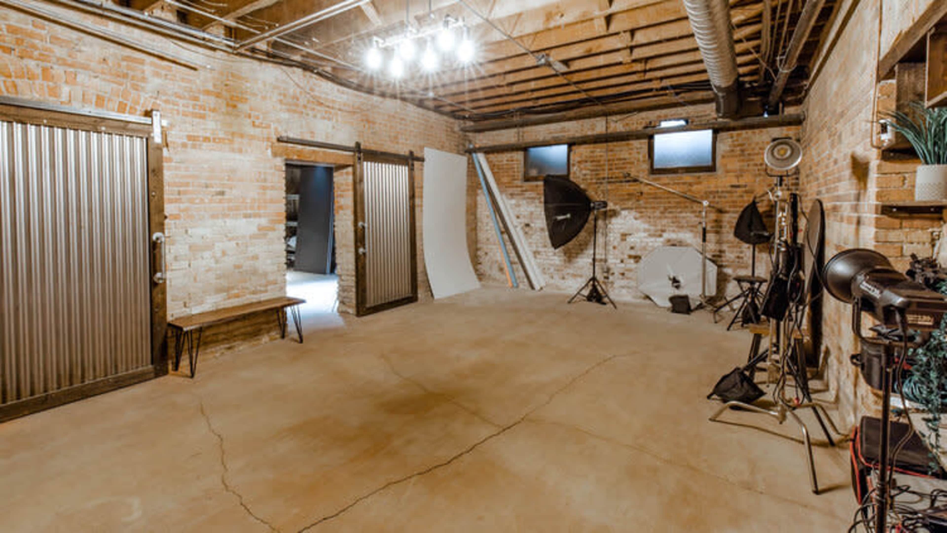 A spacious, well-lit photography studio featuring brick walls, a concrete floor, and various equipment set up for shooting.