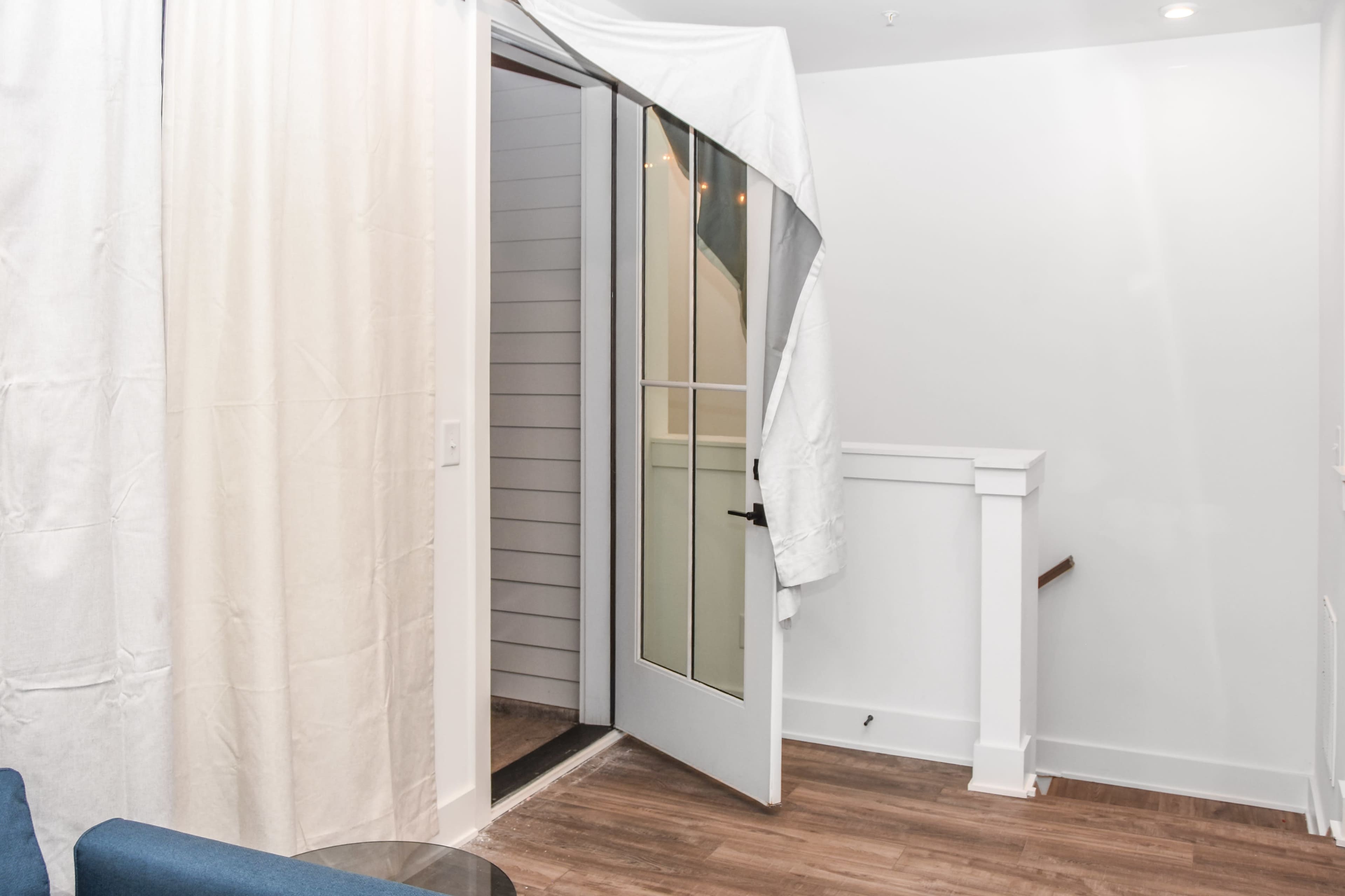 A partially open door is draped with a white cloth, revealing a small entryway with wooden flooring and a visible staircase.