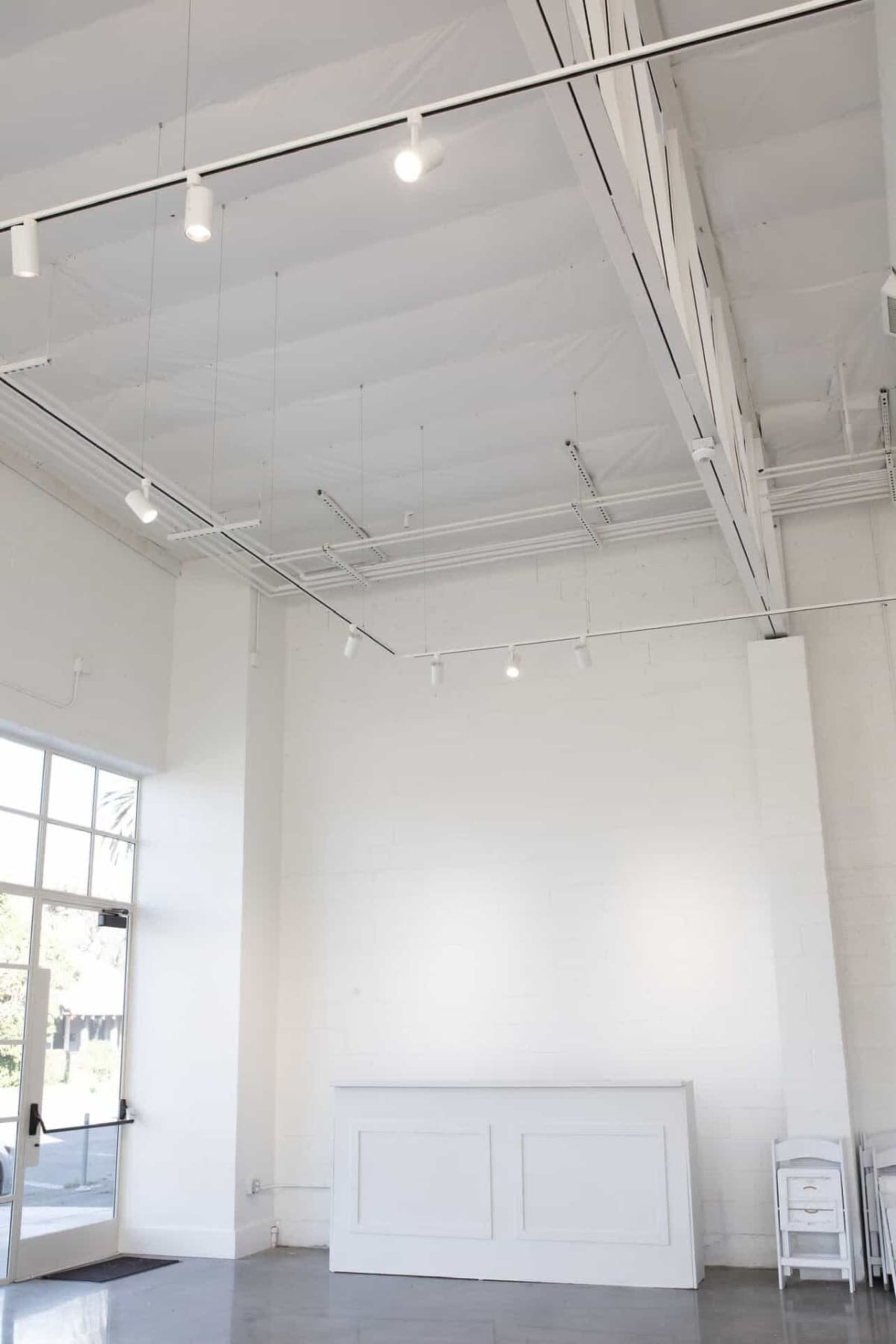 The image depicts a bright, minimalist interior space with a white wall, a reception counter, and hanging lights.