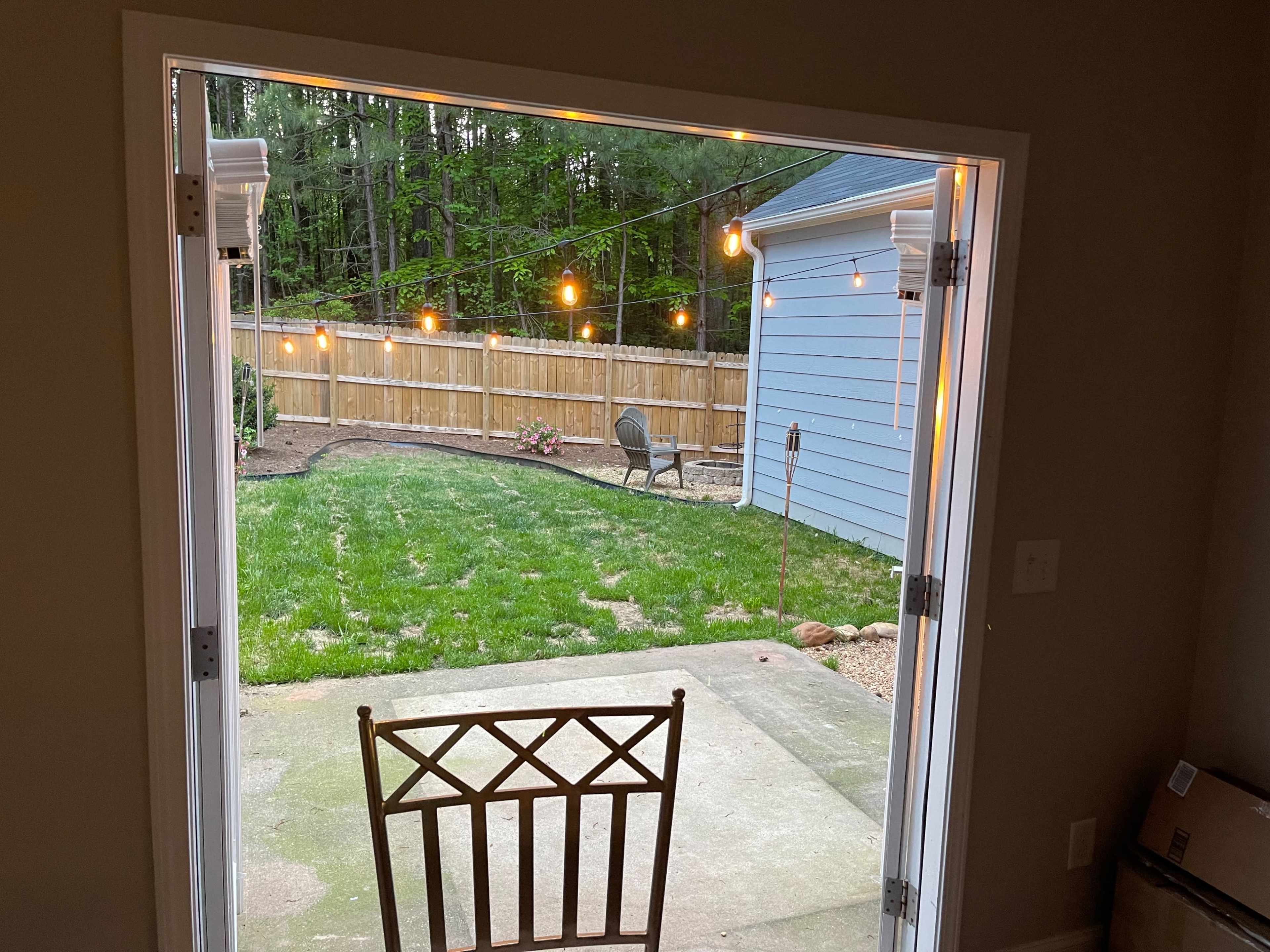 A chair is positioned at an open doorway looking out onto a backyard with string lights and landscaped areas.