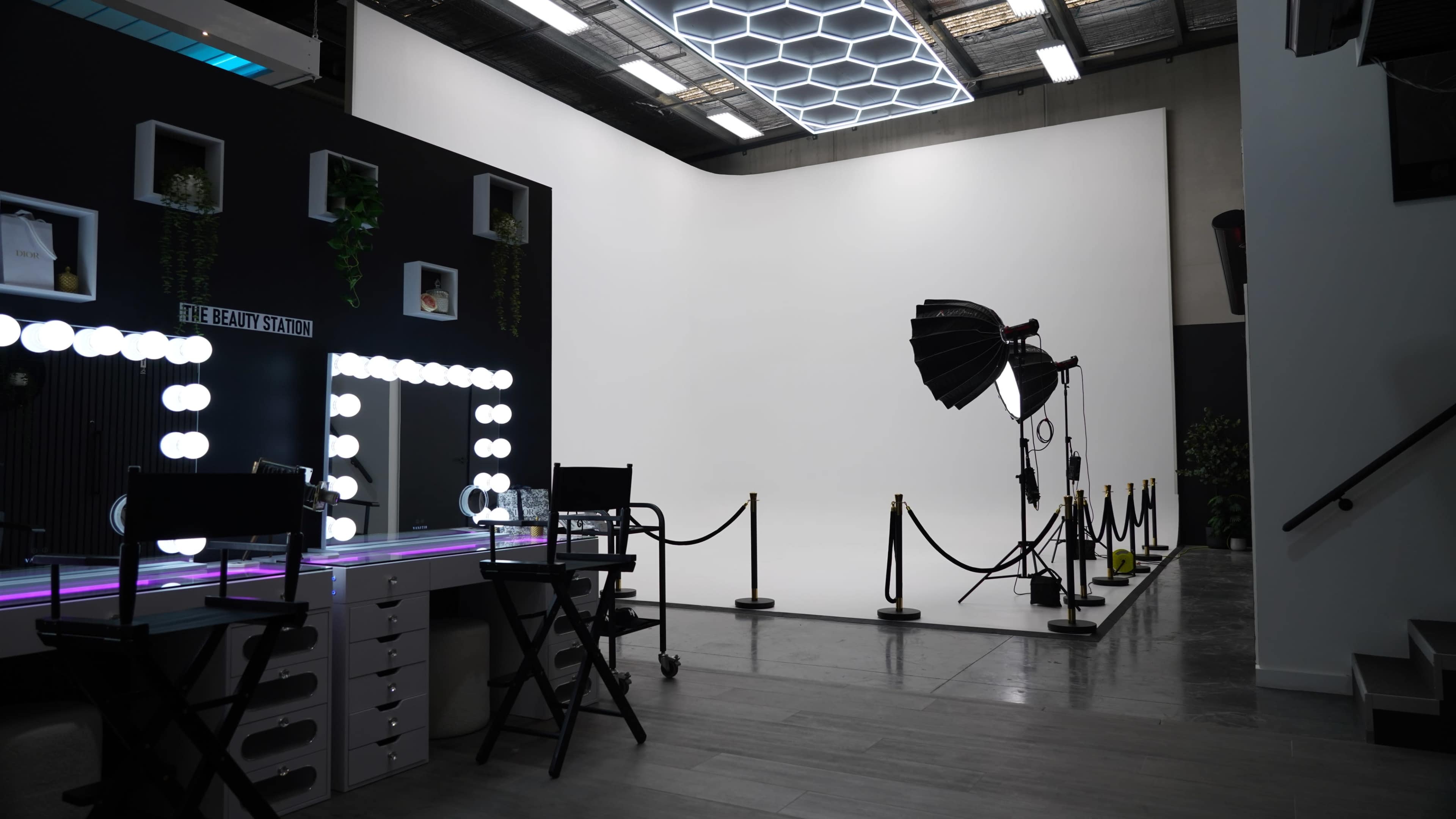 The image shows a modern photography studio featuring a vanity with illuminated mirrors, a large backdrop area, and studio lighting equipment.