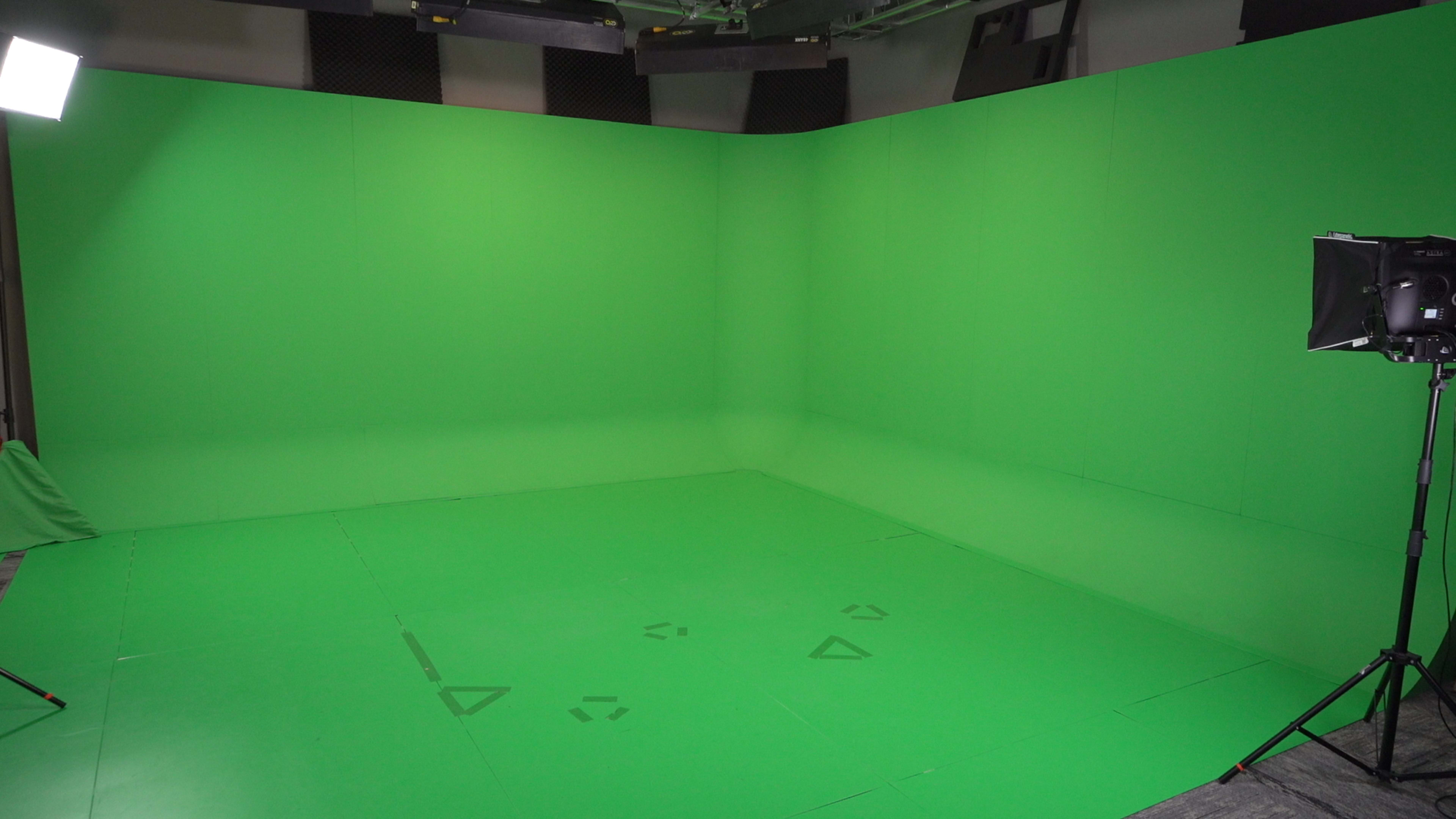The image shows a green screen studio with green walls and flooring, equipped with lighting on one side.