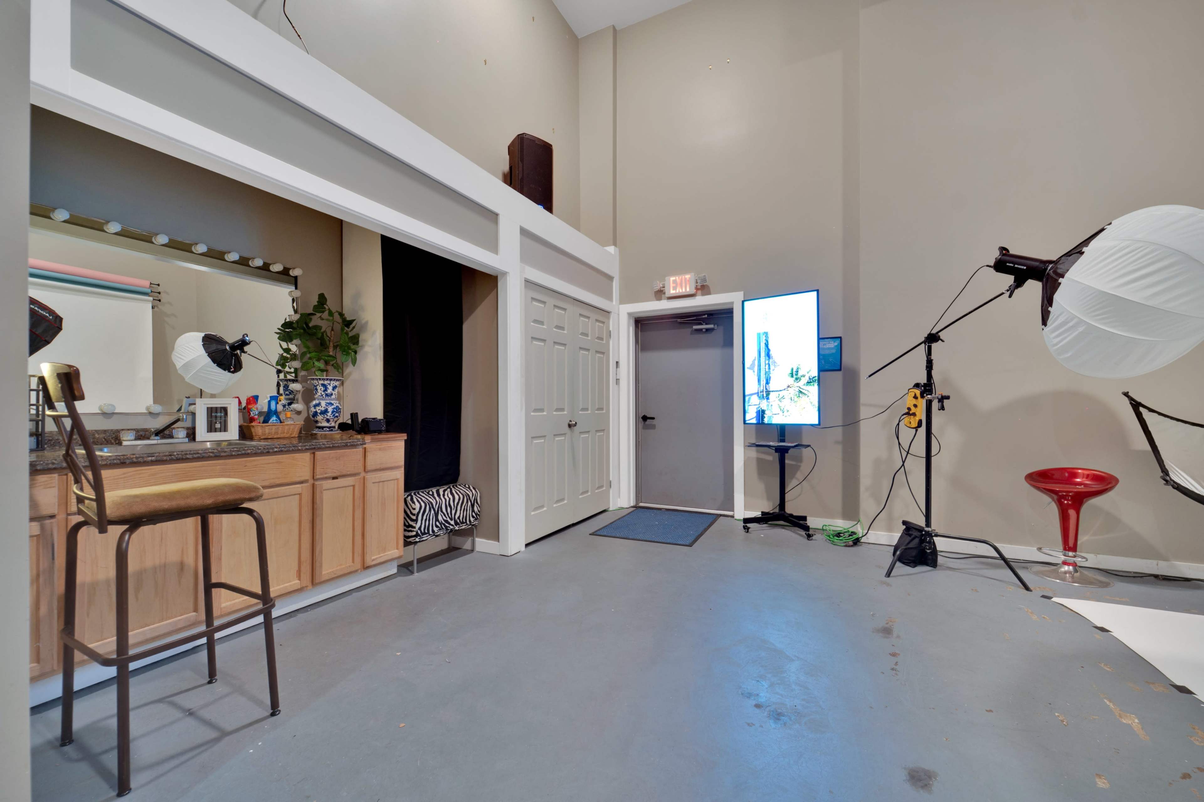 The image shows a studio interior with a vanity area on the left, a closed door on the right, and a large screen displaying an image in the center.