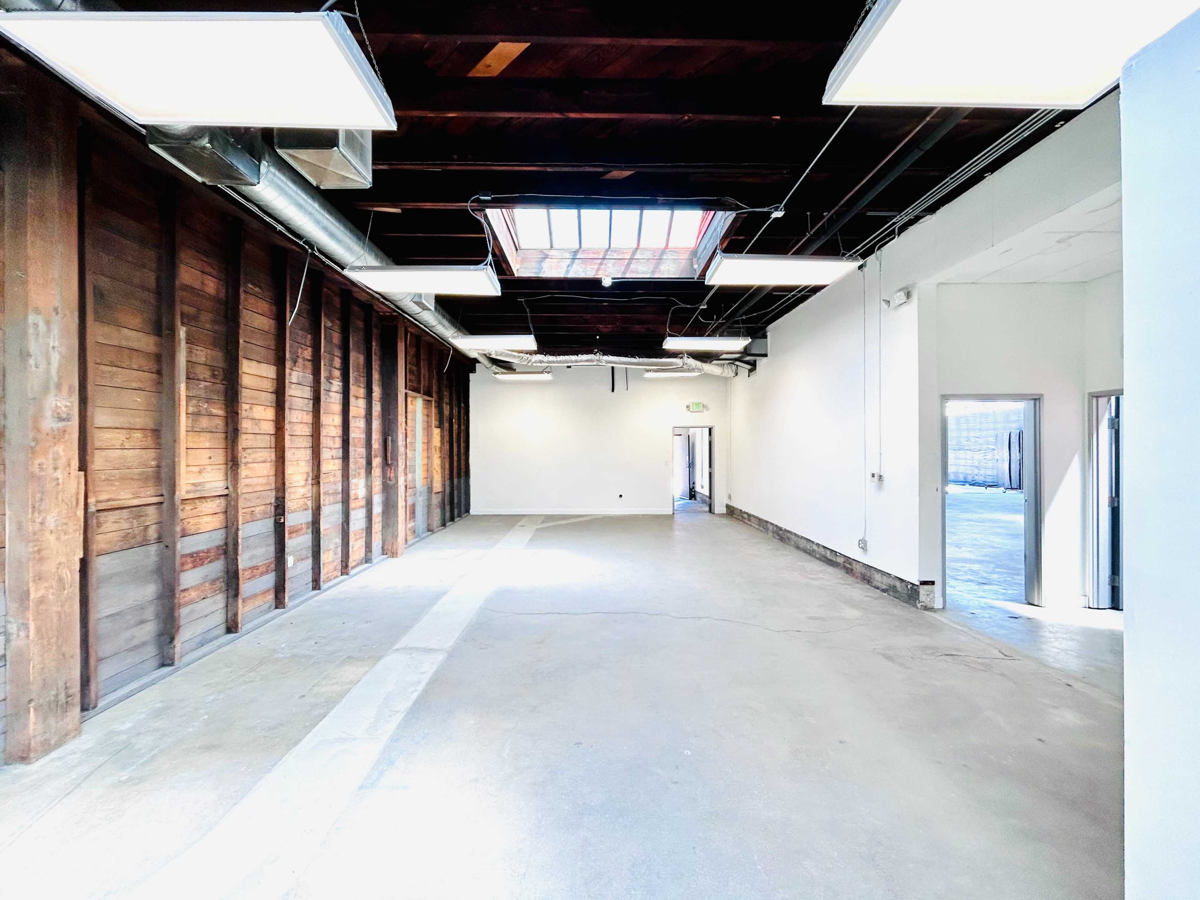 The image shows an empty interior space with wooden walls, concrete flooring, and overhead lighting.