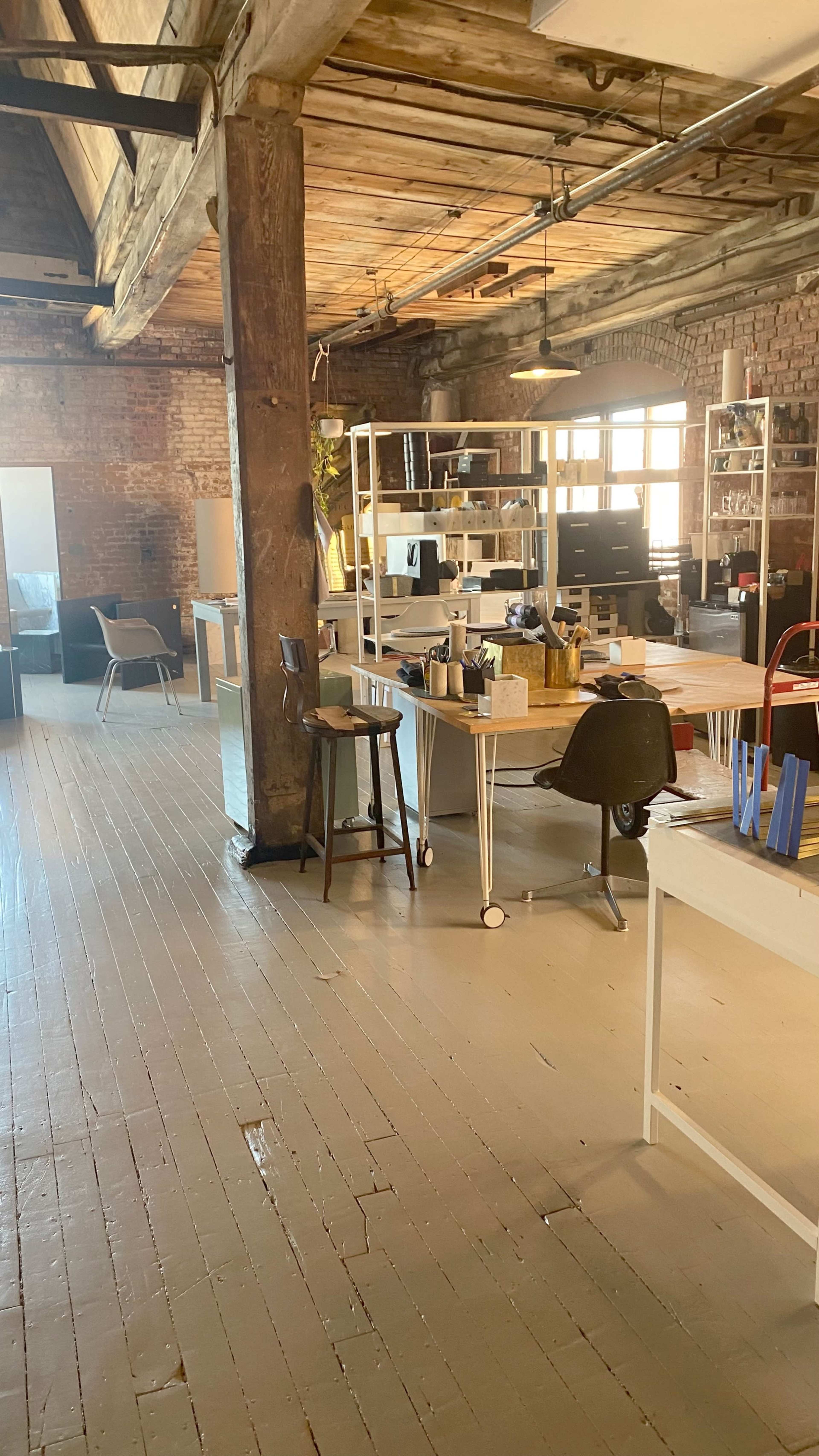 An open office space with wooden beams, light-colored flooring, various workstations, and large windows letting in natural light.