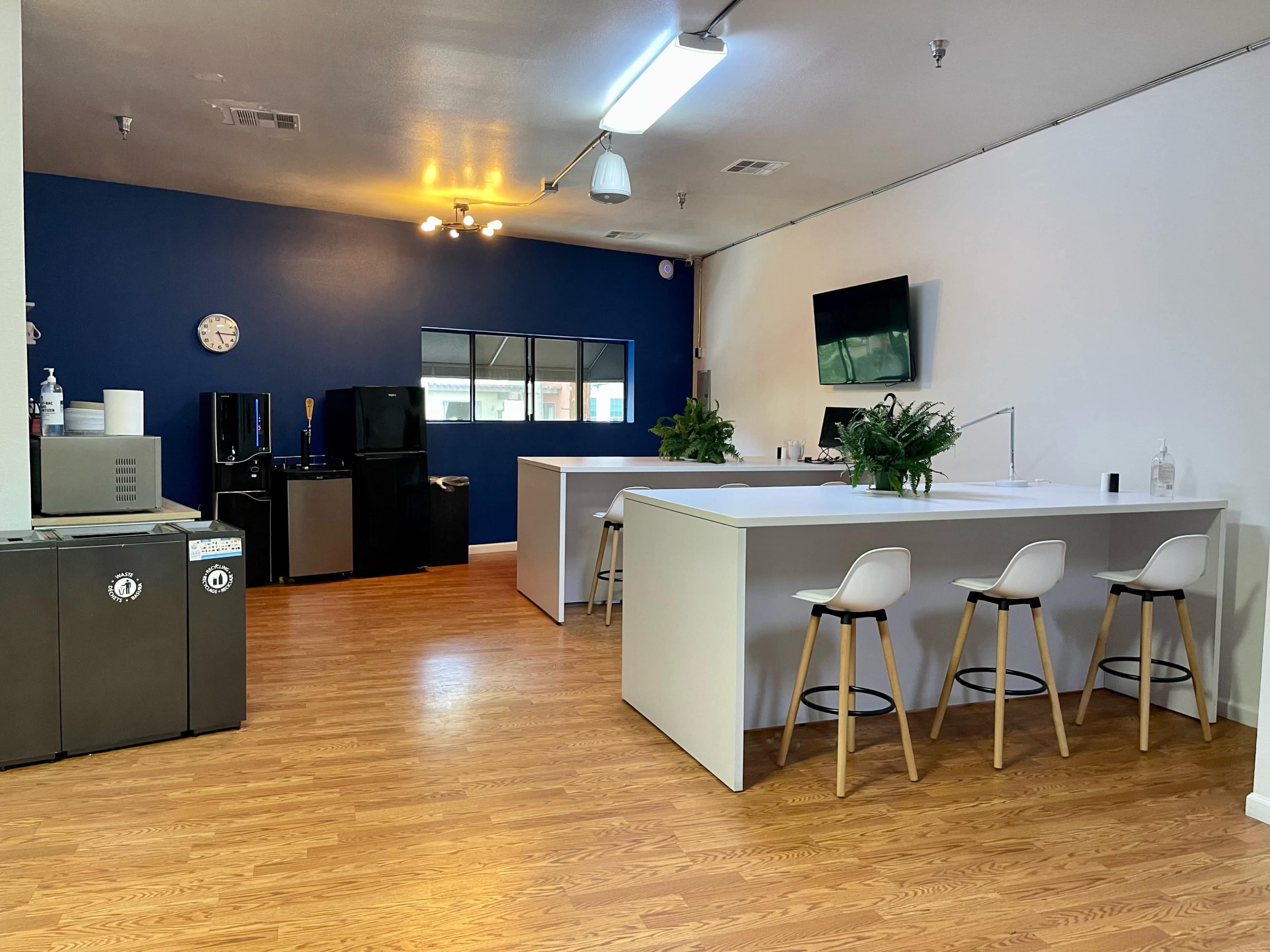 A modern kitchen area with a white island counter, three stools, and dark cabinets along one wall, set against a blue and white color scheme.