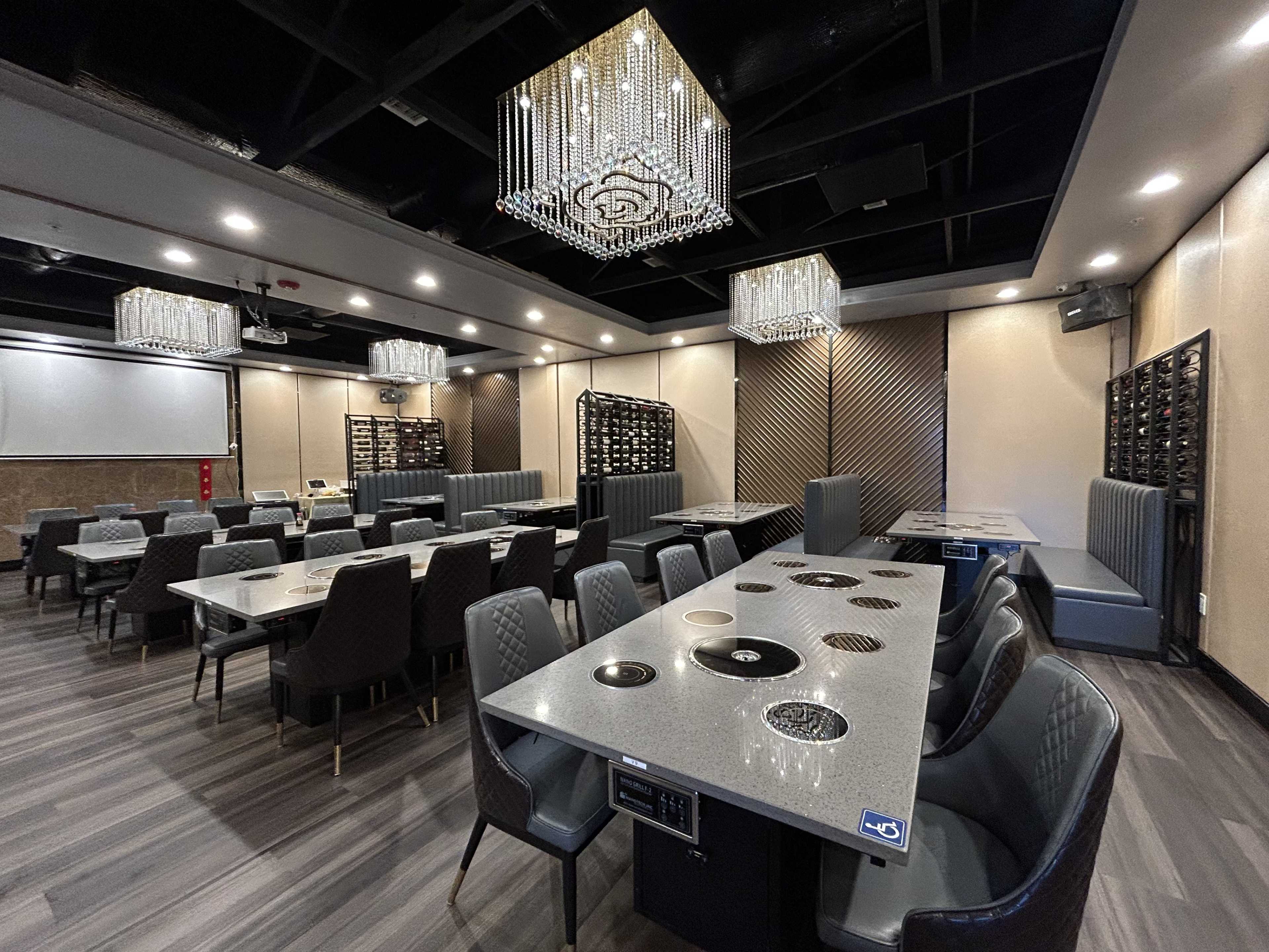 A spacious, modern restaurant interior with gray tables, plush seating, and elegant chandeliers.