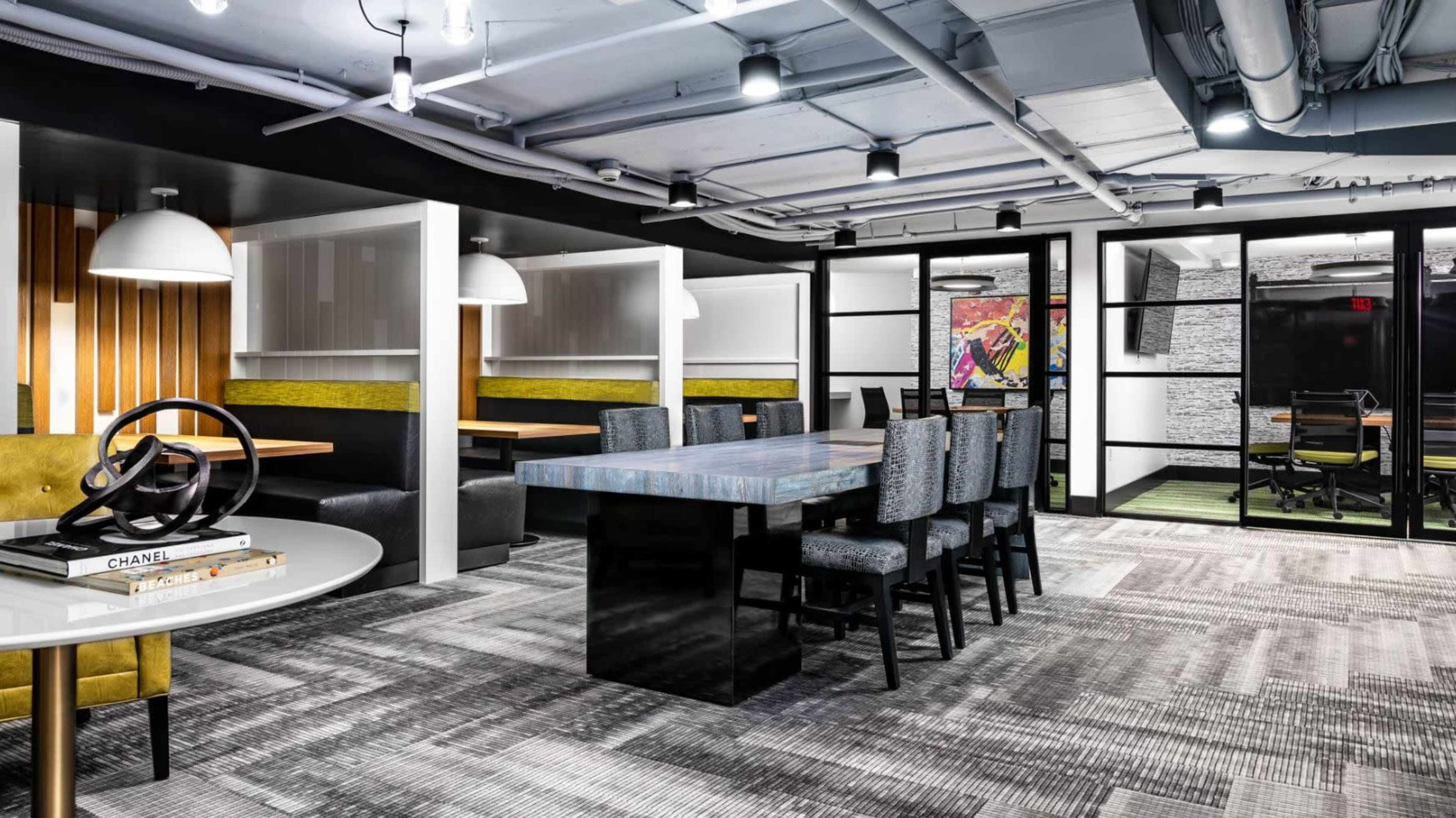 A modern workspace featuring a mix of seating areas, including booths and a large table, with stylish decor and ambient lighting.