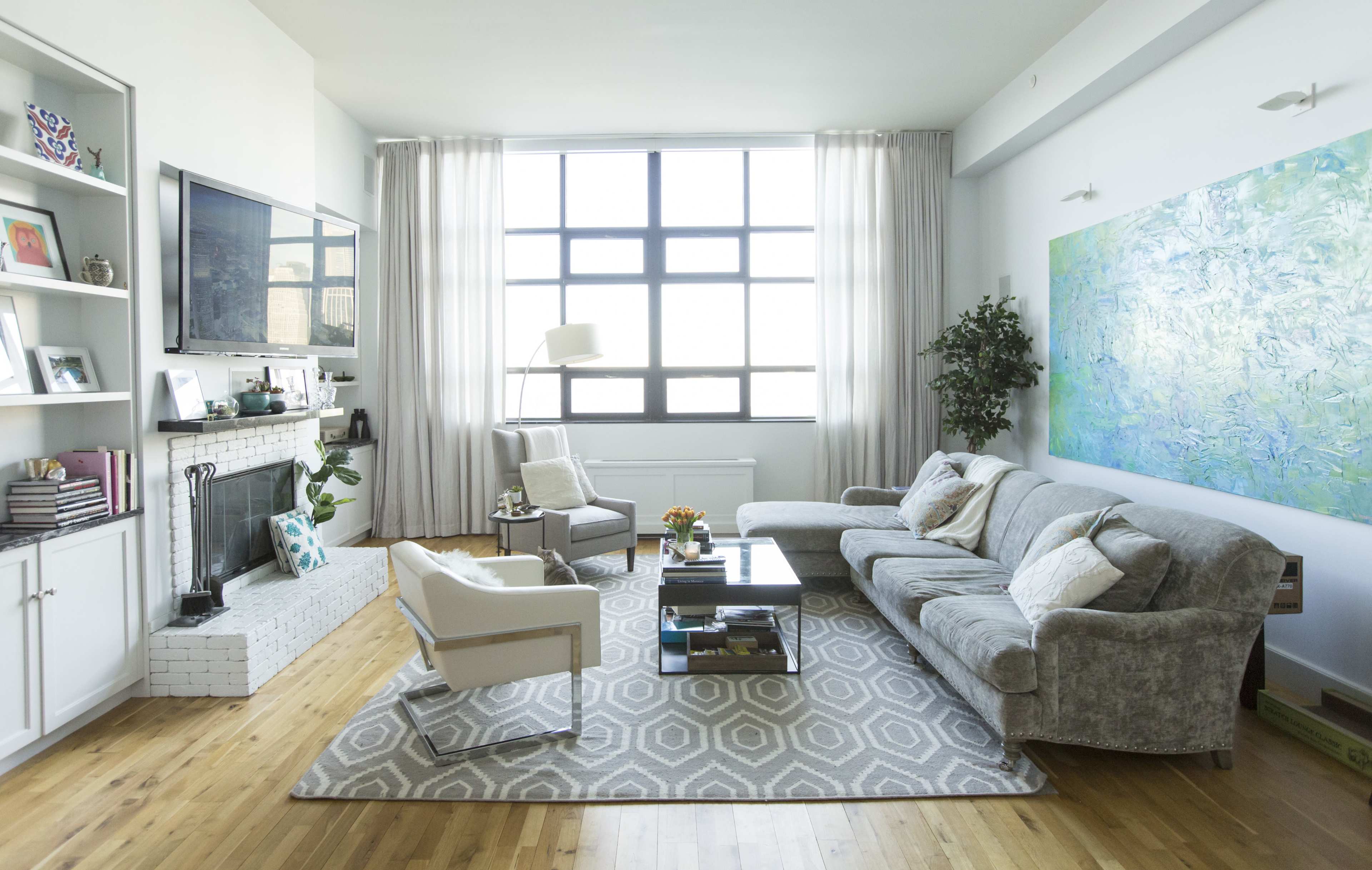 A modern living room with a large window, a gray sectional sofa, a coffee table, and a green abstract painting on the wall.