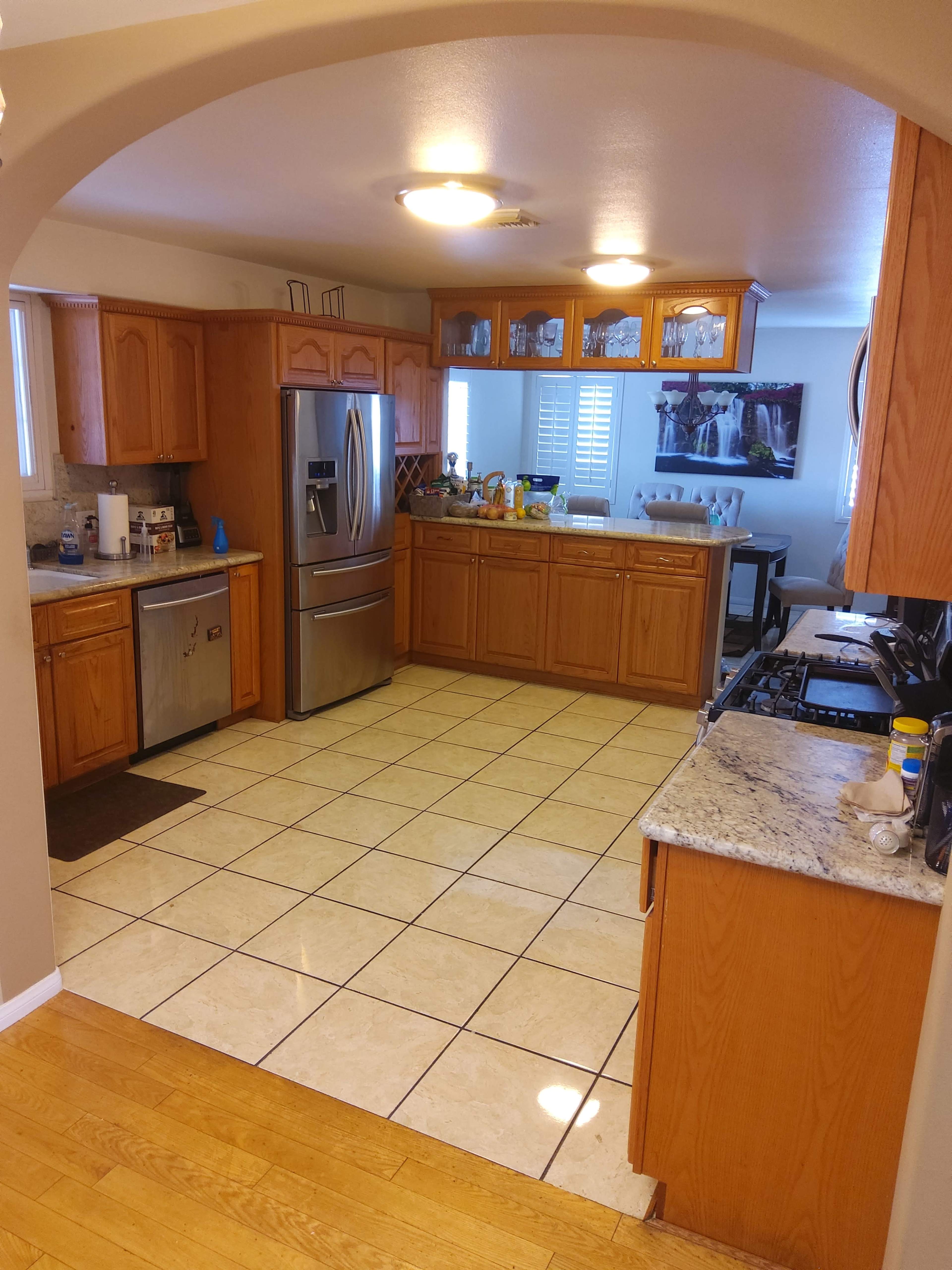 The kitchen features wooden cabinets, stainless steel appliances, tiled flooring, and a dining area with a view of the adjacent room.