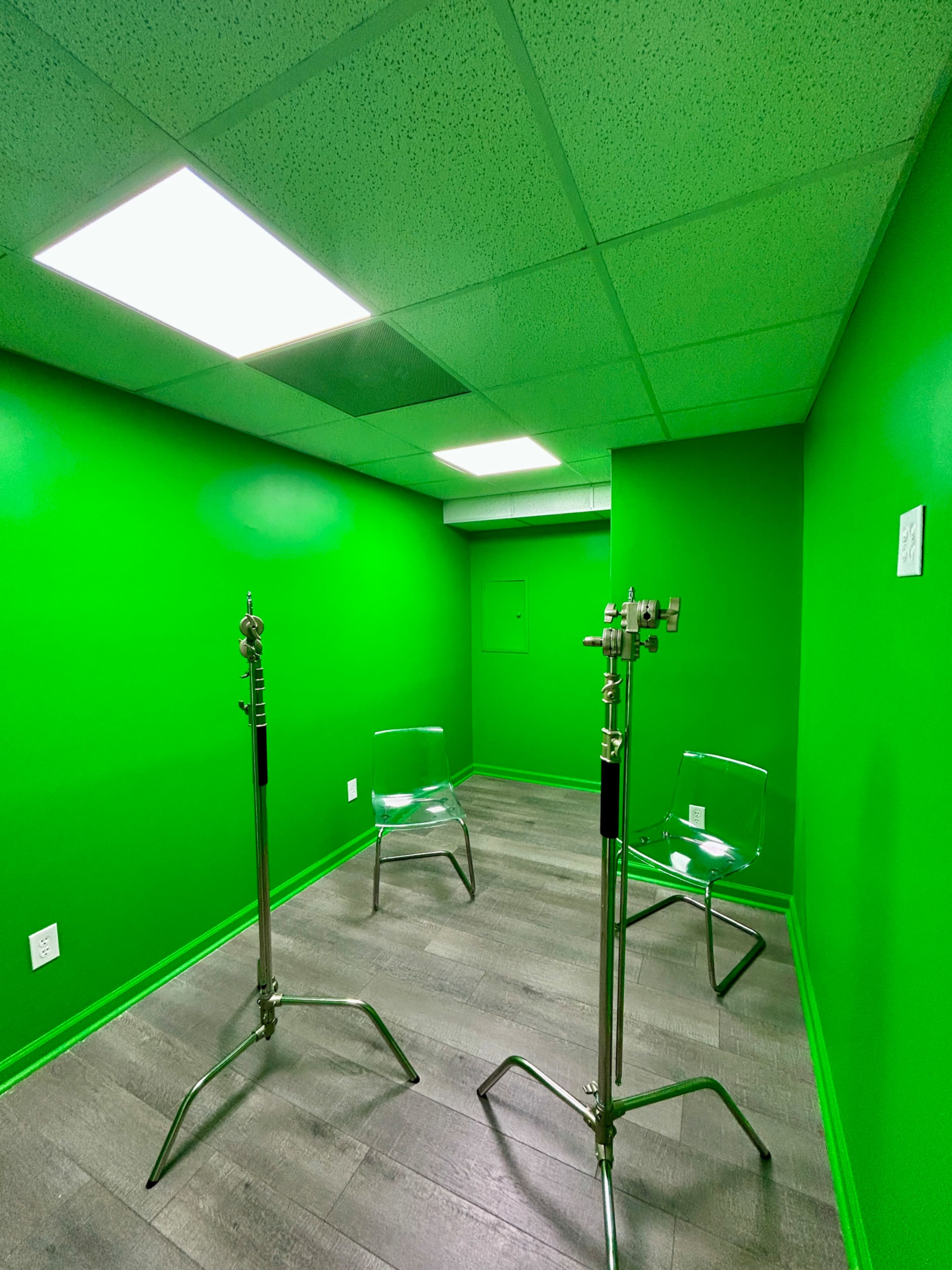 The image shows a small room with bright green walls and three clear chairs arranged around two metal stands.