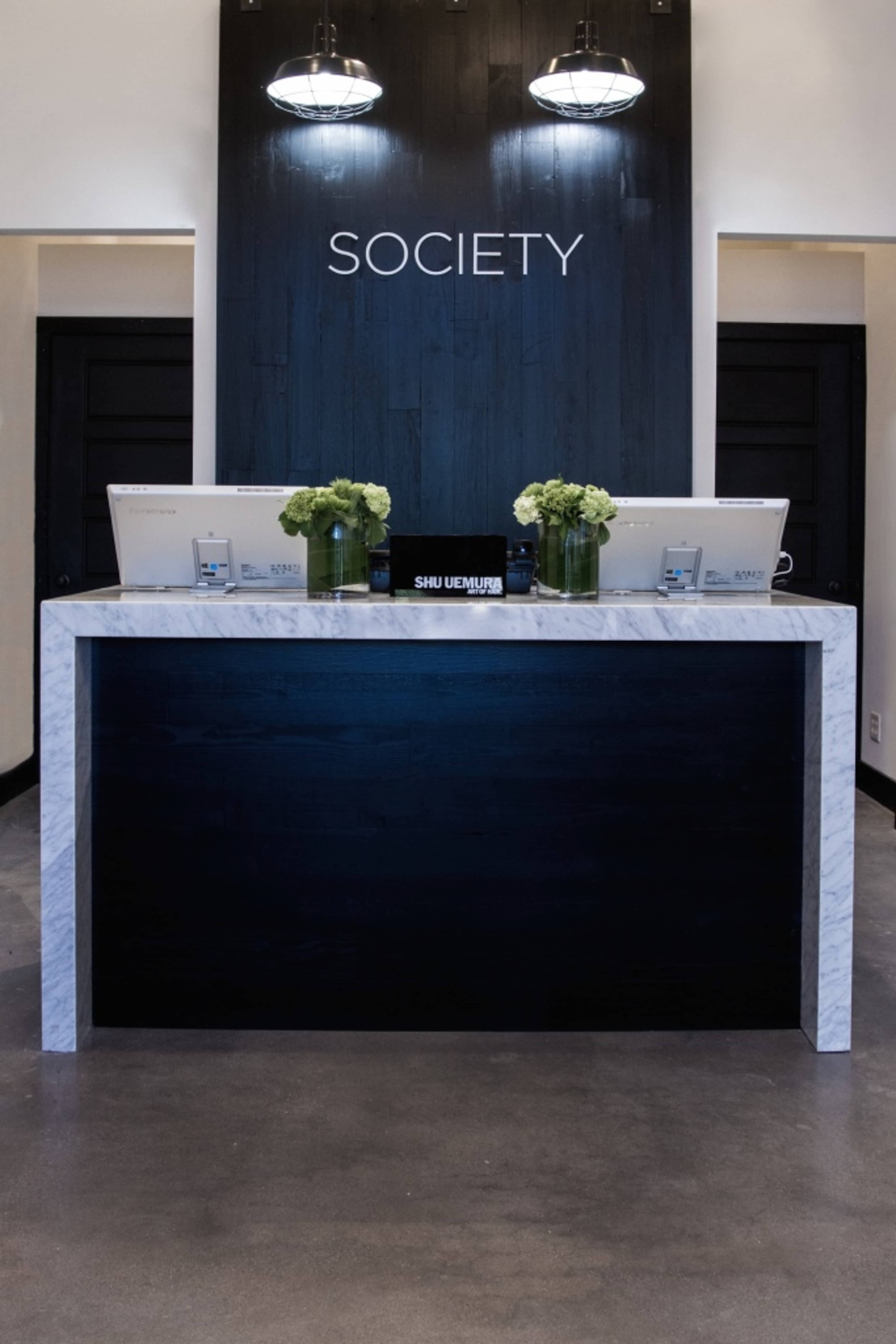 A modern reception desk with a marble countertop and two computer stations, featuring the word "SOCIETY" displayed above.