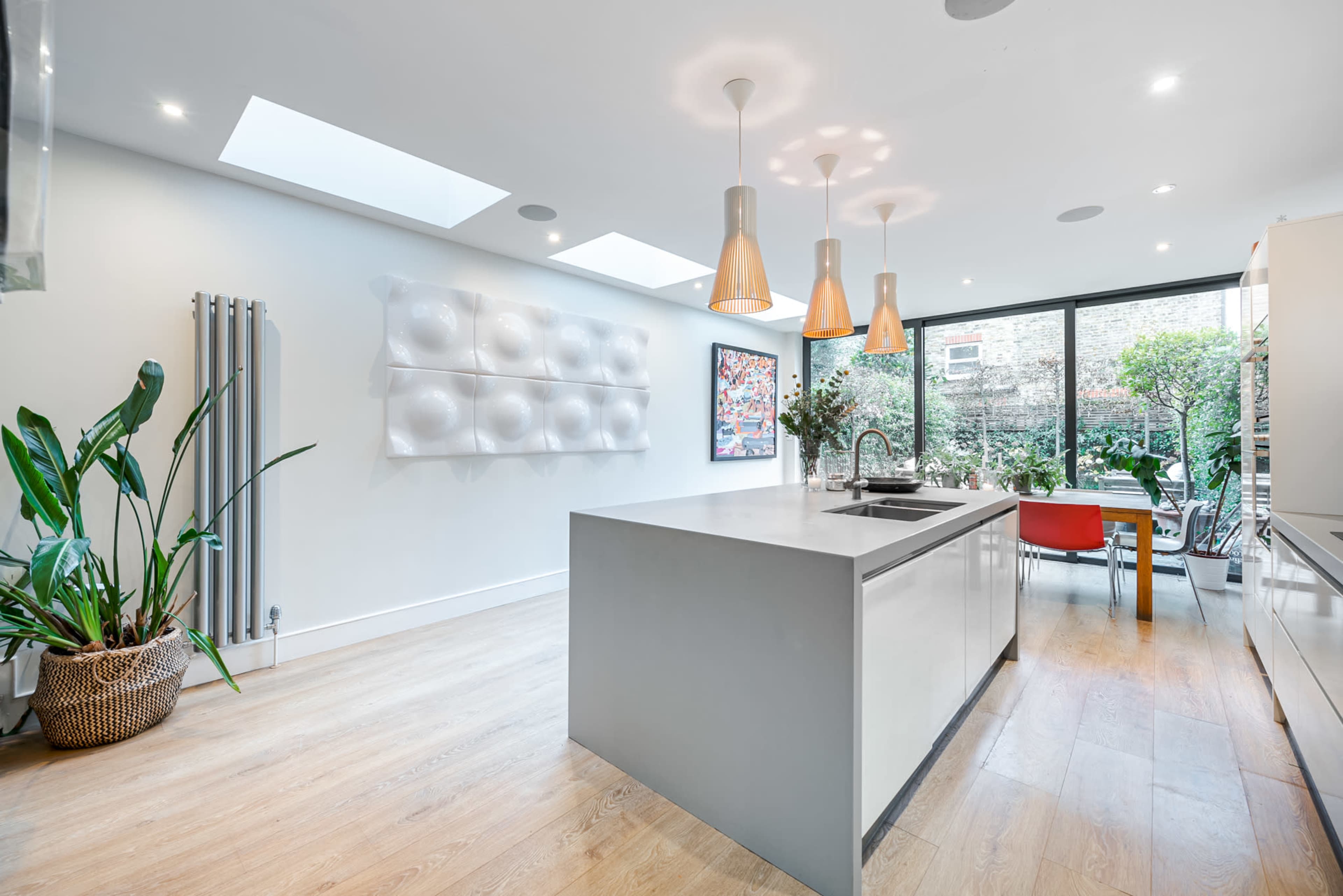 A modern kitchen features a large island, pendant lighting, and large windows overlooking a garden.