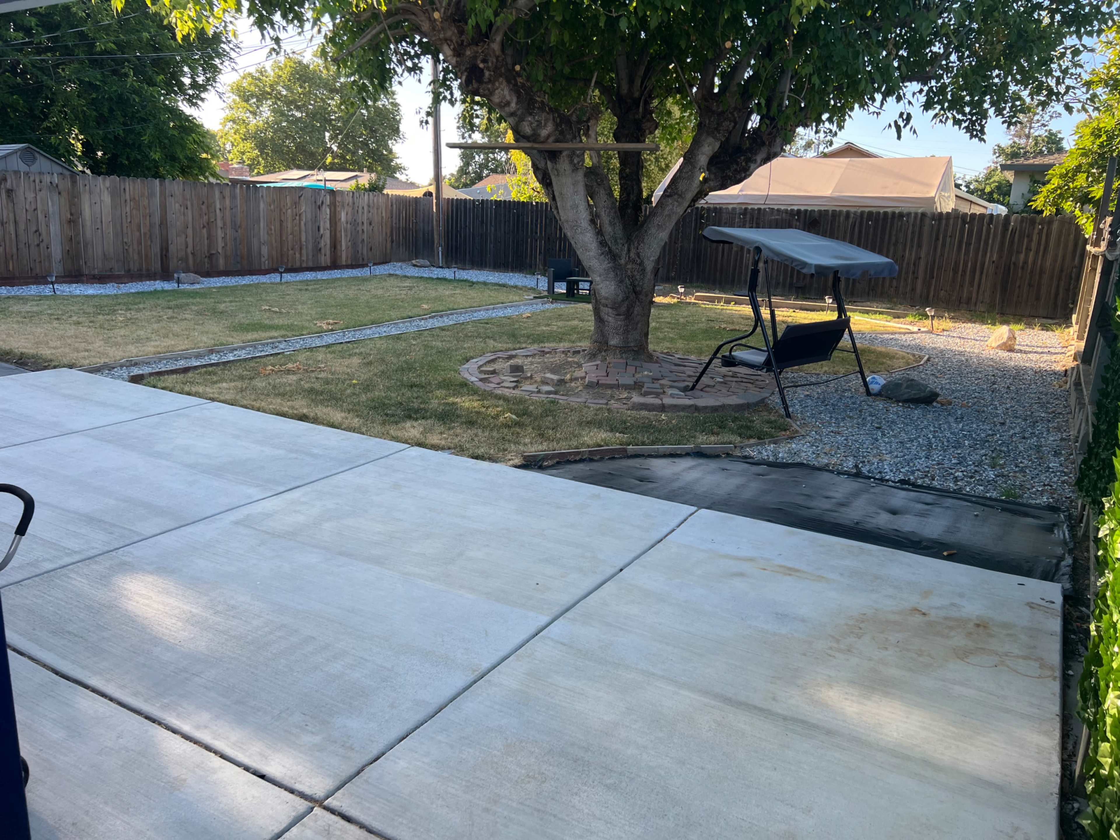 A backyard with a grass area, a stone path, a swing chair under a tree, and a gravel border.