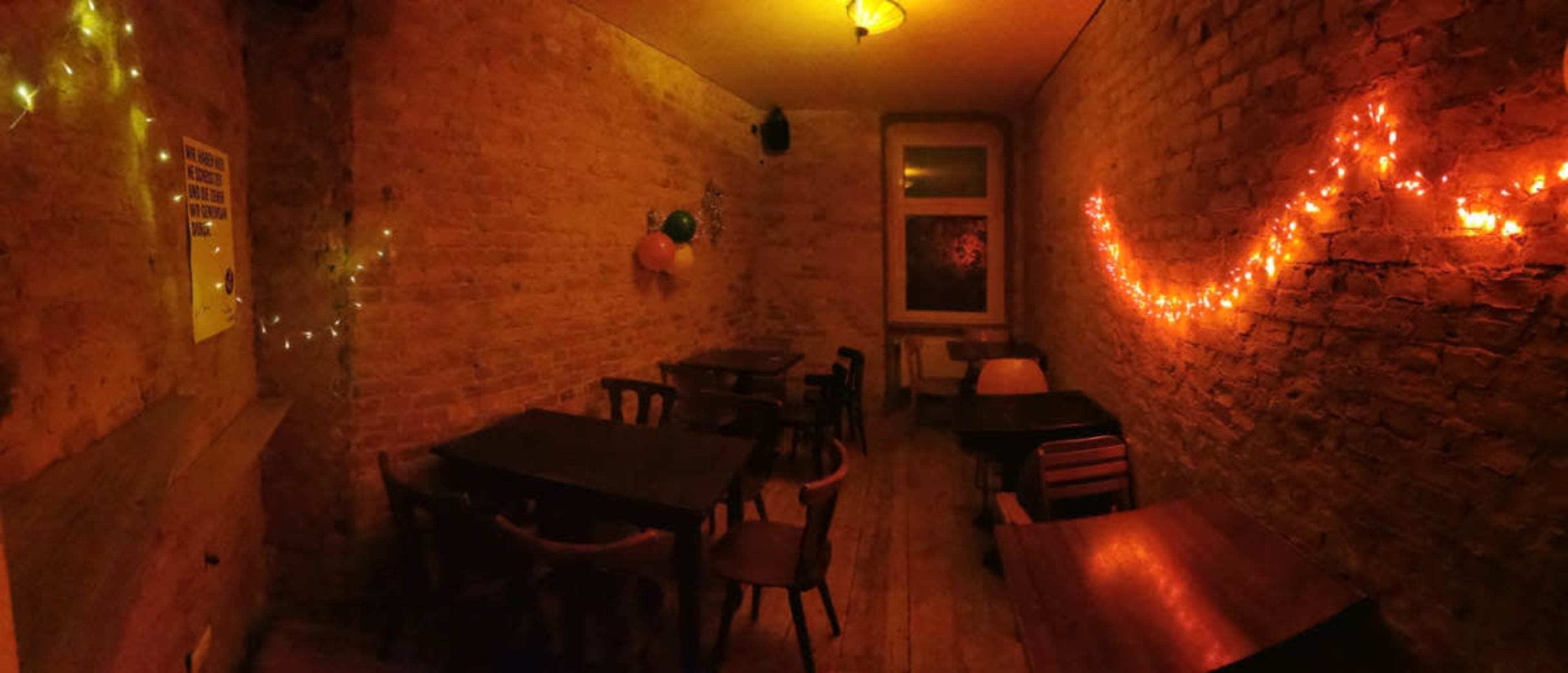 The image shows a dimly lit, empty room with brick walls, several wooden tables, and string lights decoratively placed.