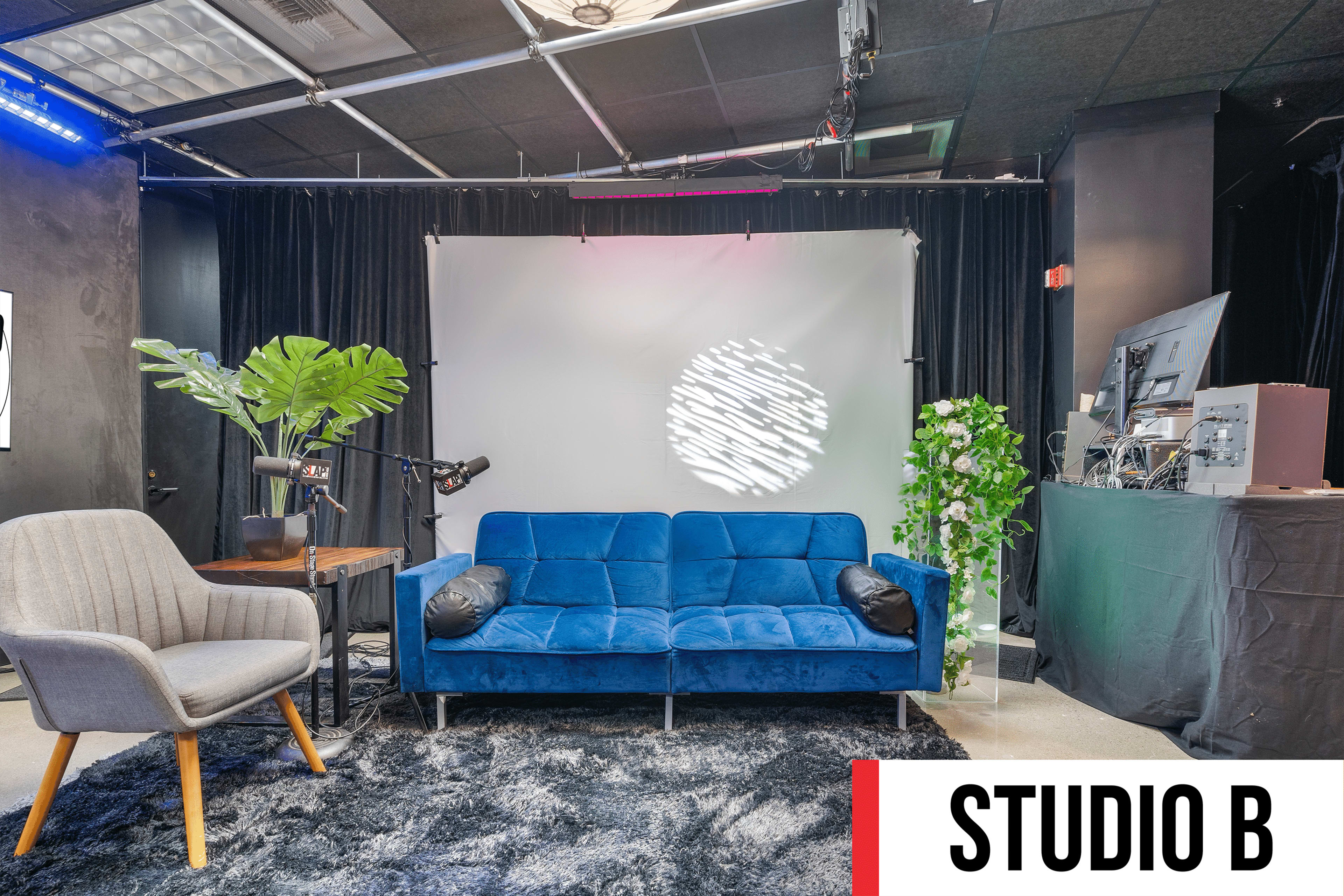 A cozy studio setup featuring a blue sofa, a side table with a lamp, a green plant, and a backdrop with soft lighting.