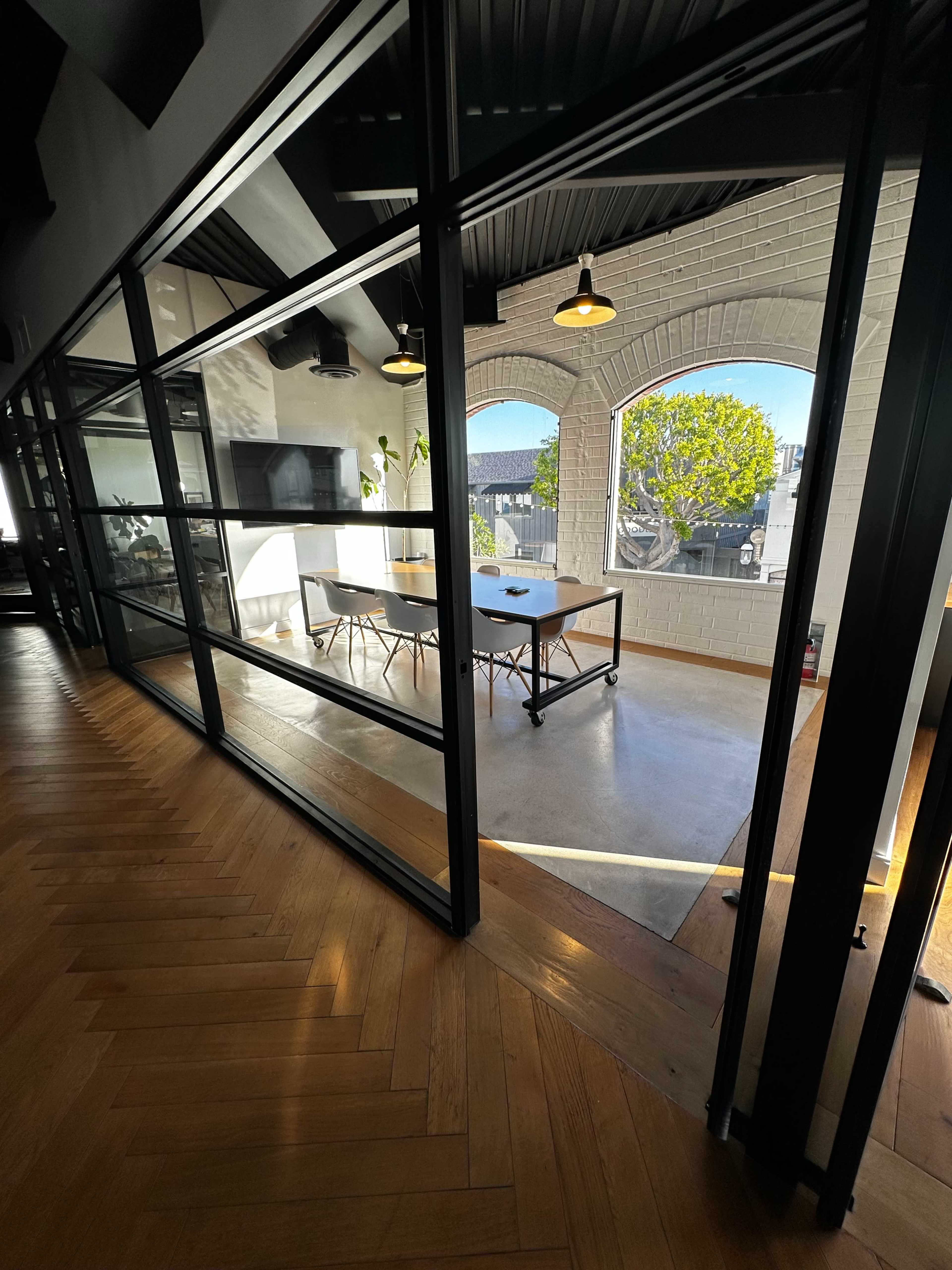 A modern conference room features a large table surrounded by chairs, with large windows letting in natural light.