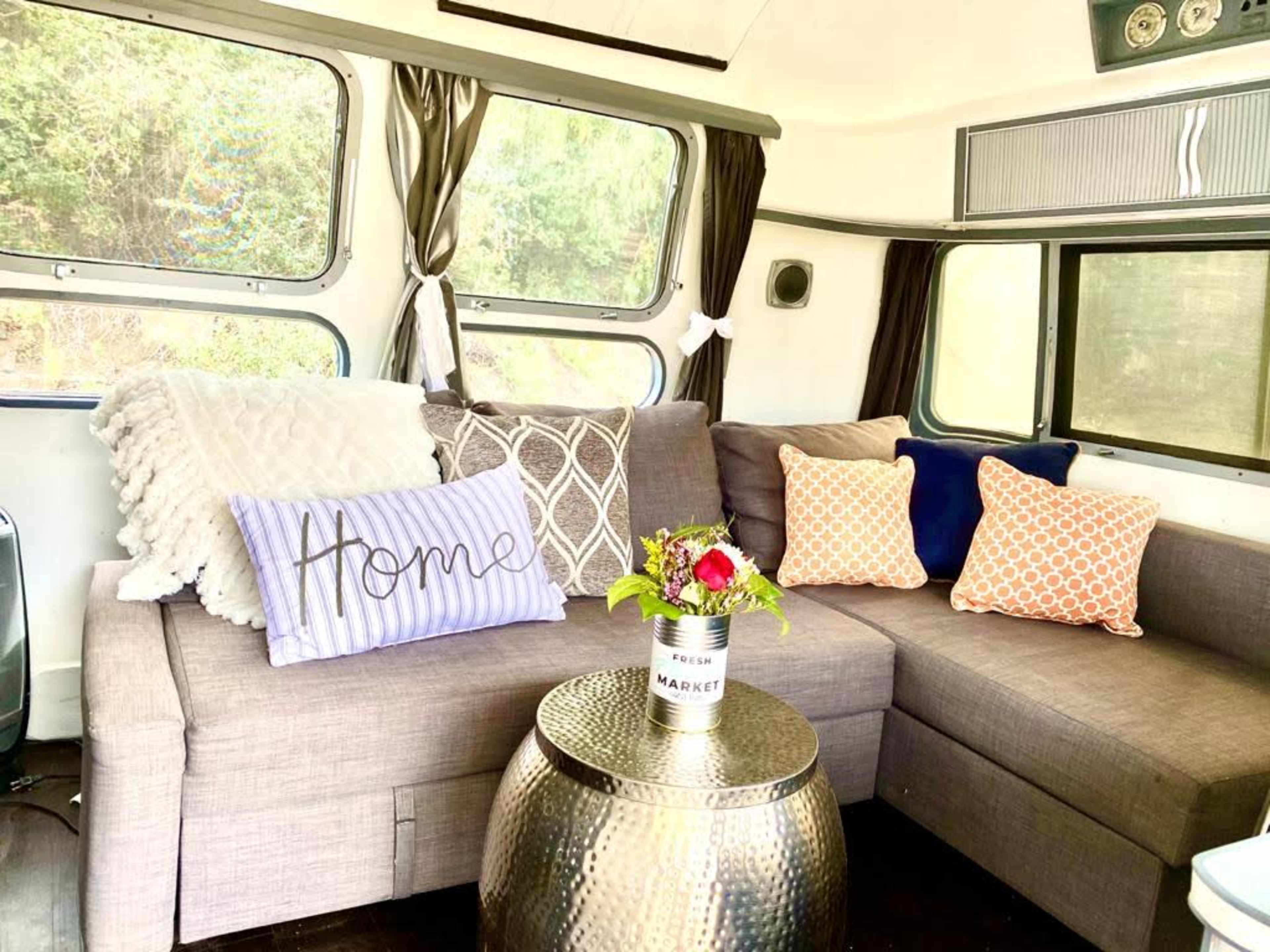 A cozy seating area features a sectional sofa adorned with decorative pillows and a small table with a floral arrangement.