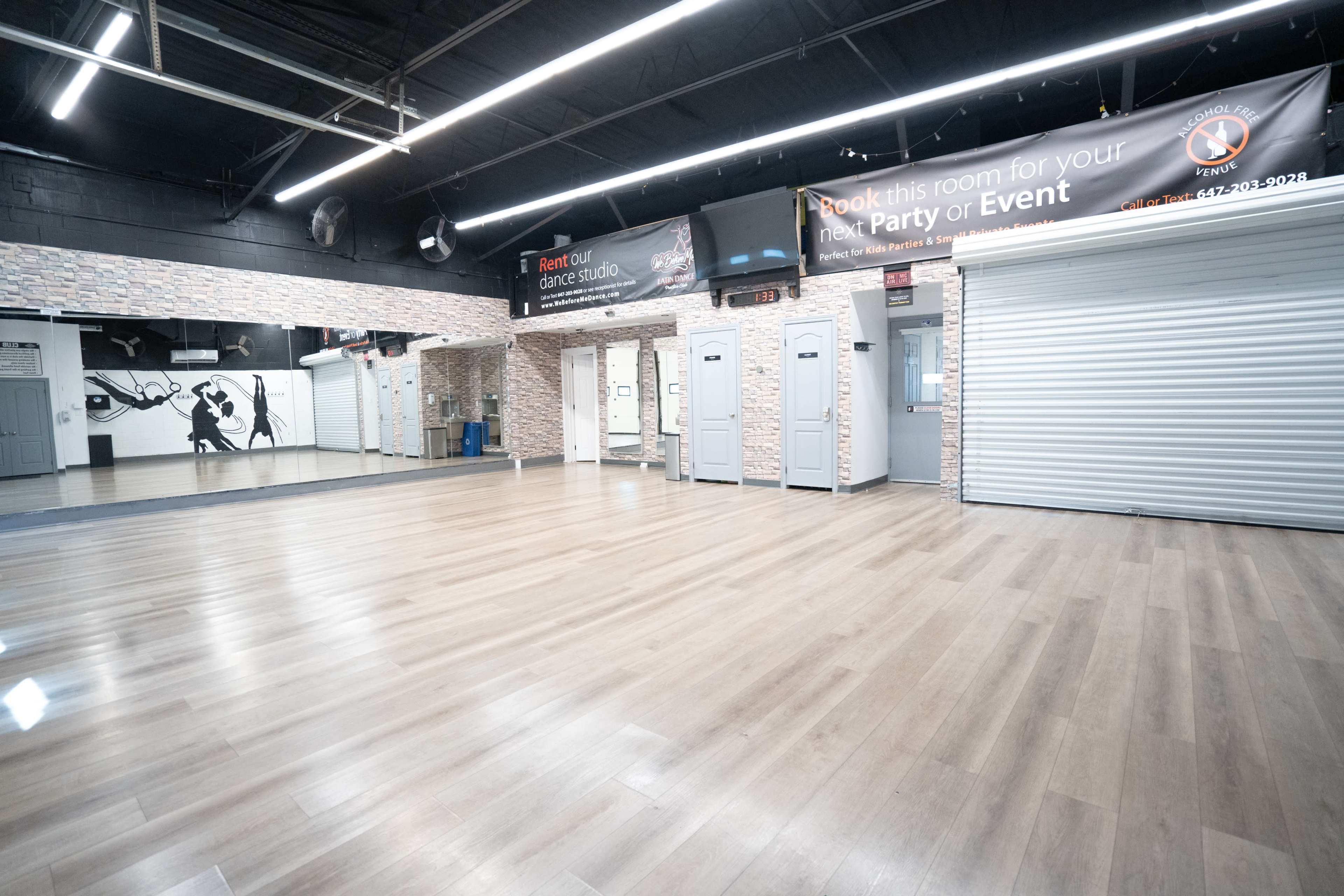 The image shows an empty dance studio with a wooden floor, large mirrors on the walls, and a banner advertising event bookings.
