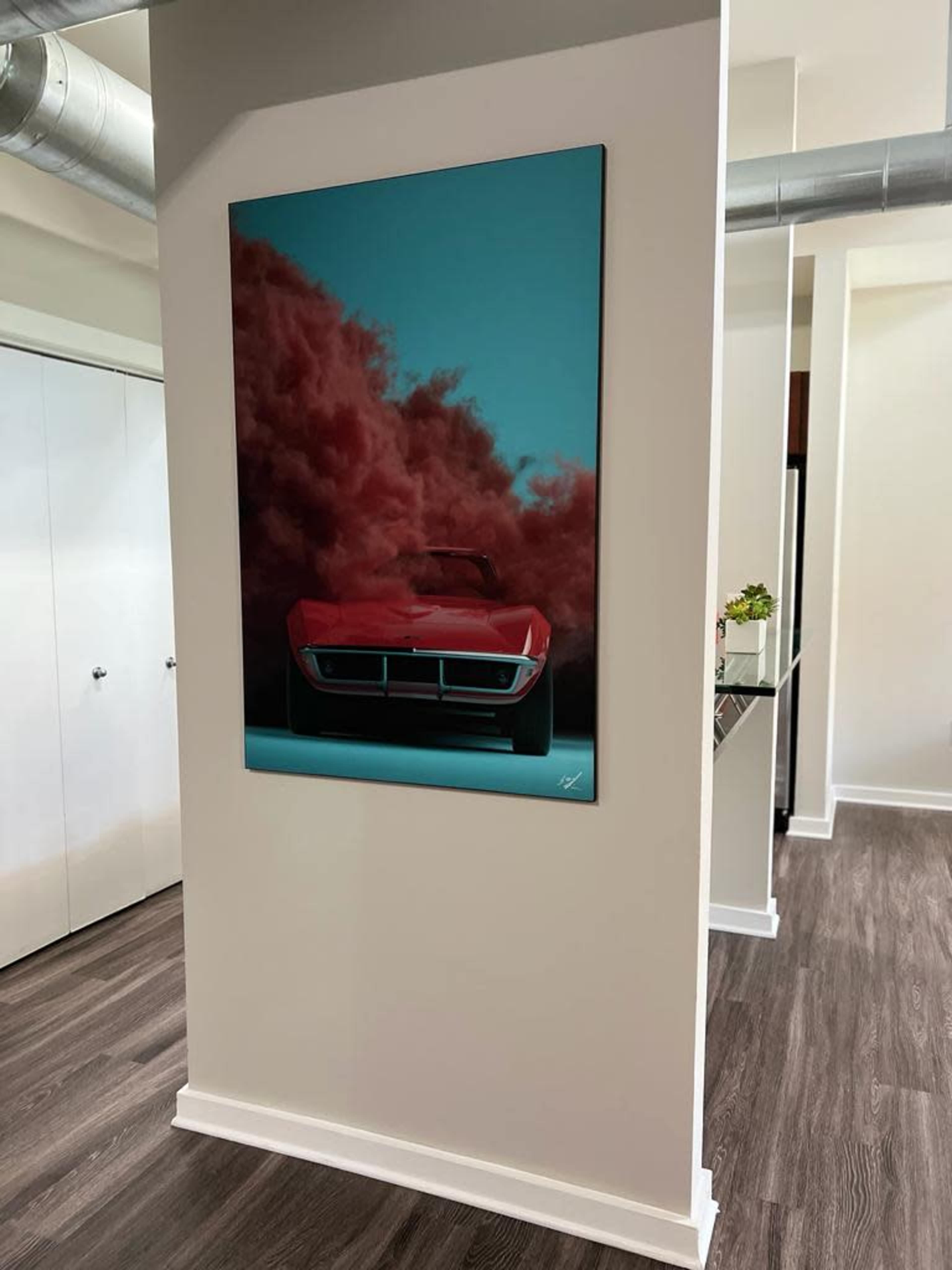A large framed artwork of a red car amidst a blue and pink cloud background is displayed on a wall in a modern interior space.