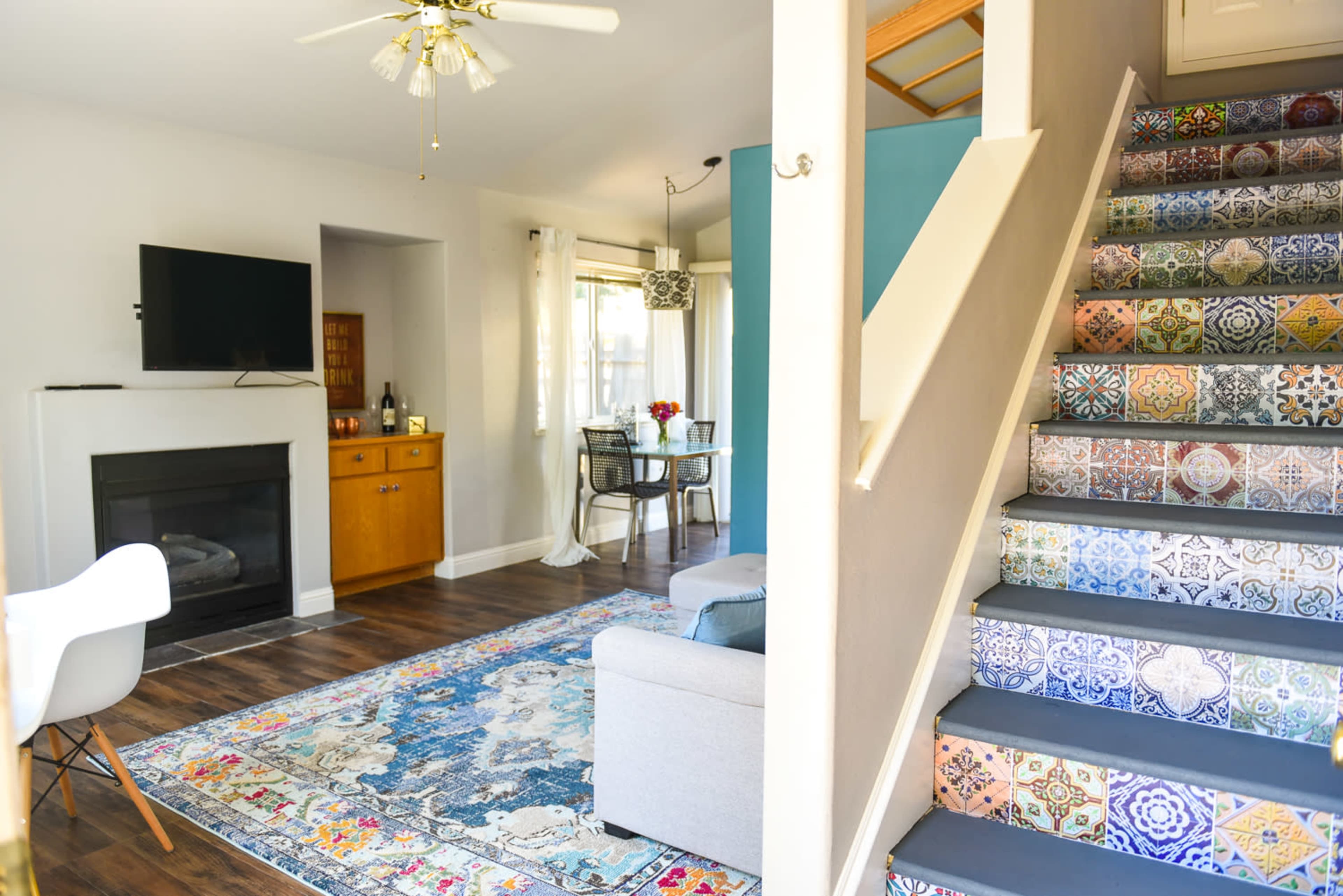 A living room with a fireplace, a television mounted on the wall, and a staircase featuring colorful patterned steps leading to an upper level.