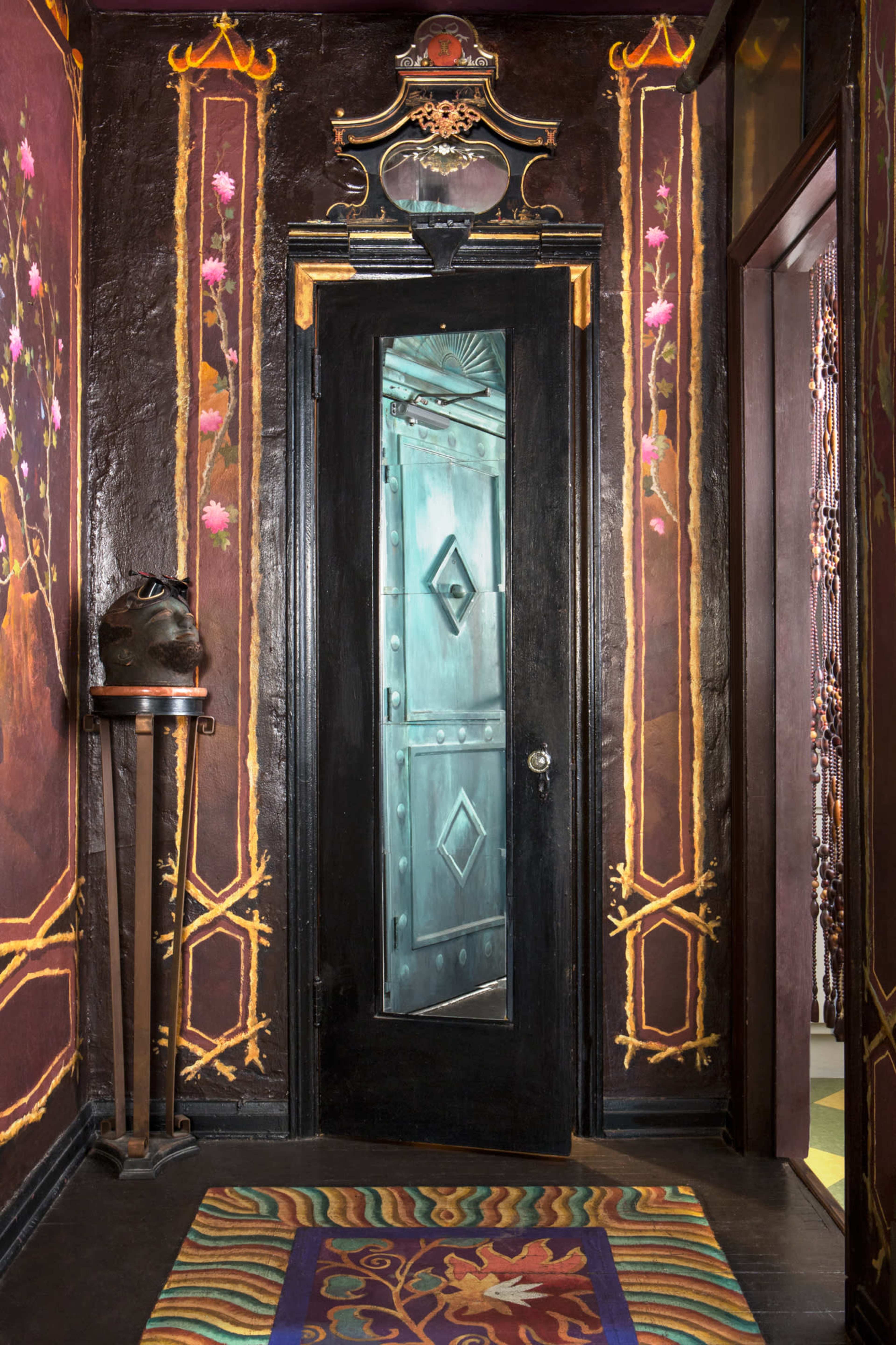 A decorative hallway features a dark door with a glass panel, surrounded by ornate wall art and a colorful rug.